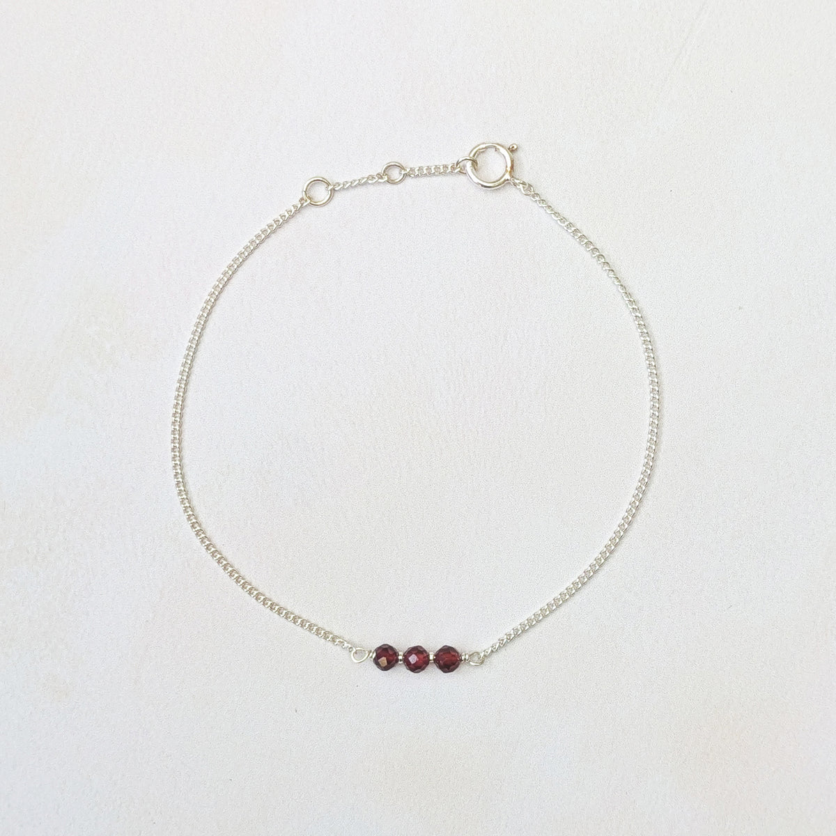 A delicate silver chain bracelet with three small, faceted Garnet beads, displayed on a clean white background.