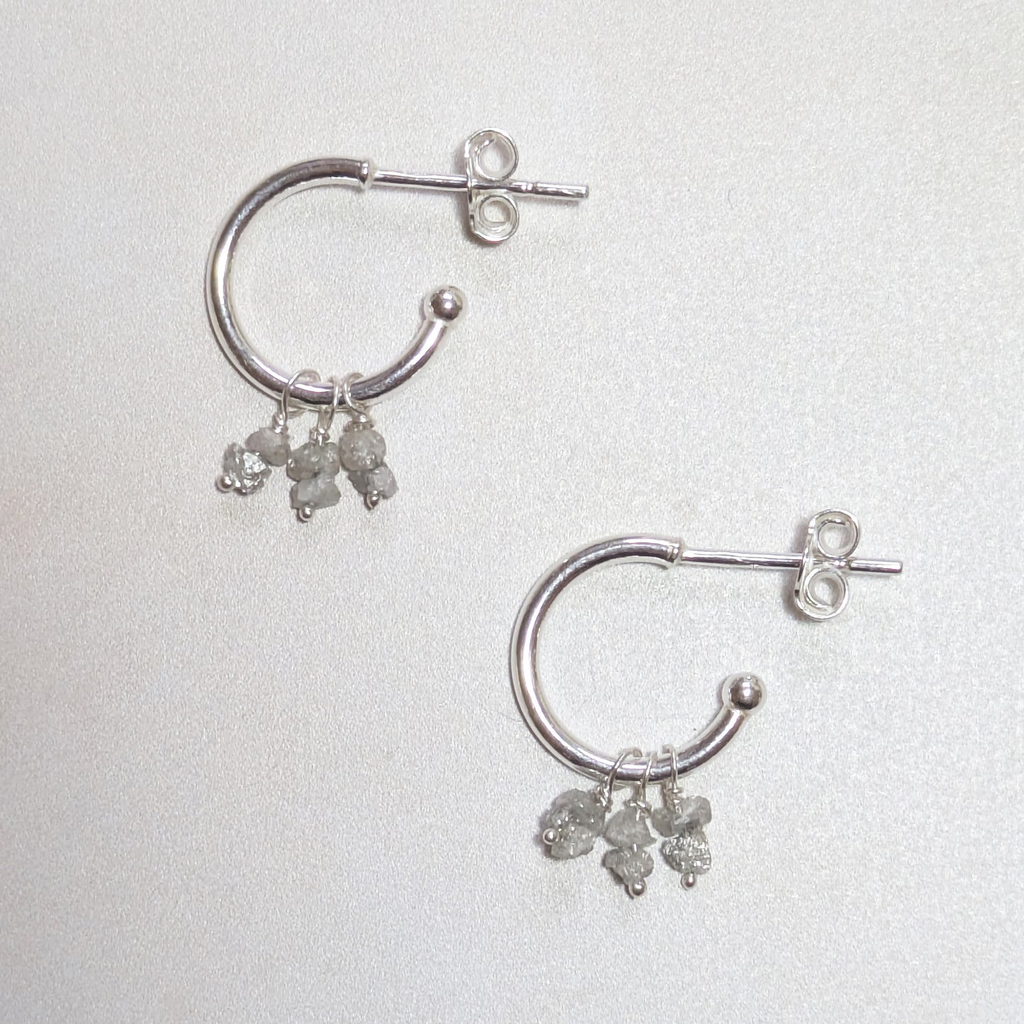 Silver hoop earrings with rough Diamond nugget gemstones on a light background.