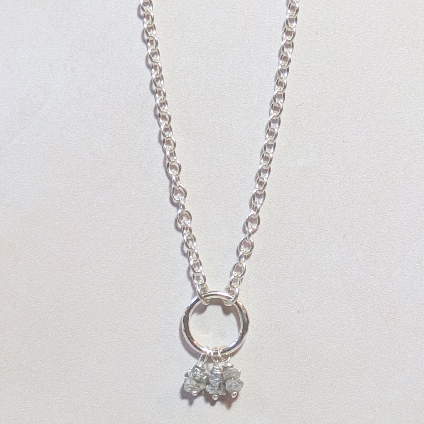 Silver necklace with a circular pendant and small rough Diamond nuggets on a light grey background.