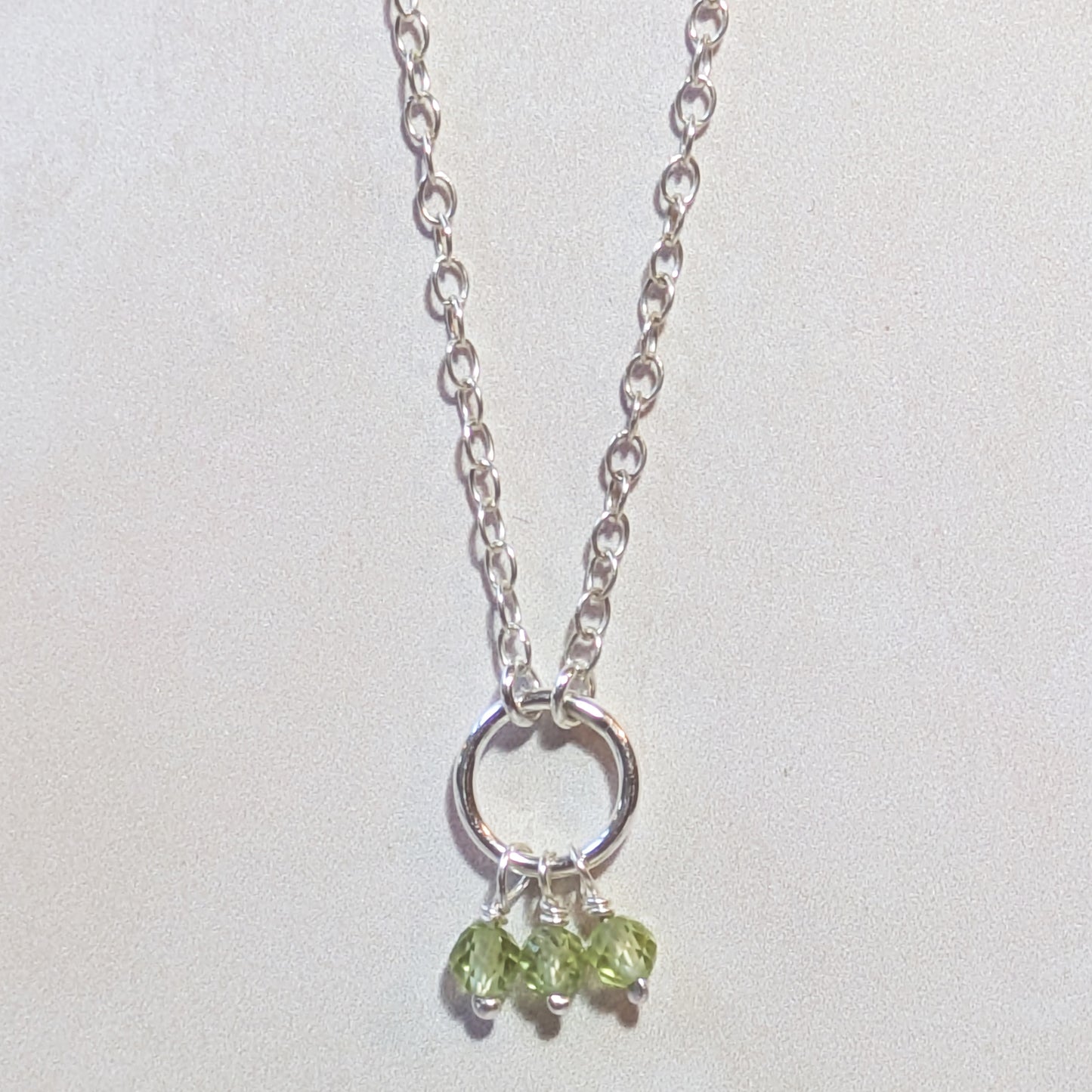 Silver necklace with Peridot gemstone beads on a light grey background.