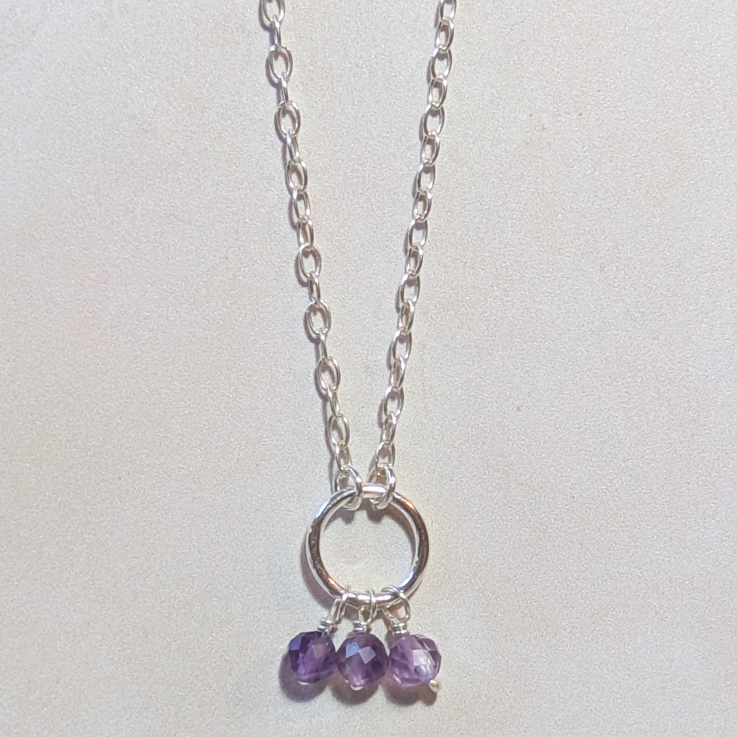 Silver chain necklace with Amethyst gemstone drops on a light grey background.