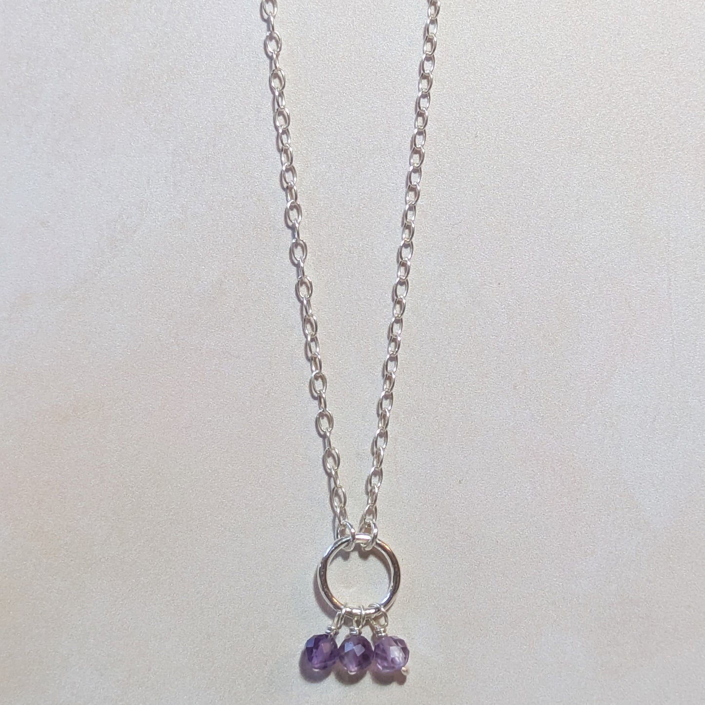 Silver circle pendant necklace with three Amethyst gemstone beads on a white background.