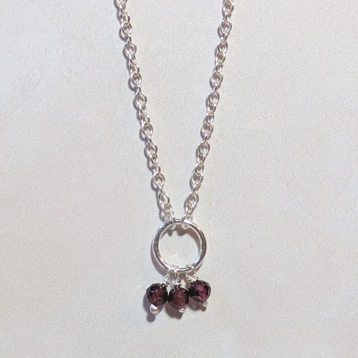 Silver necklace with three Garnet gemstone beads on a light grey background.