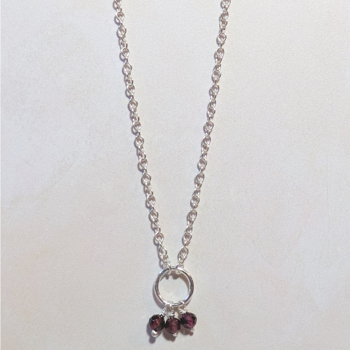 Silver necklace with circular pendant and Garnet gemstone beads on a white background.