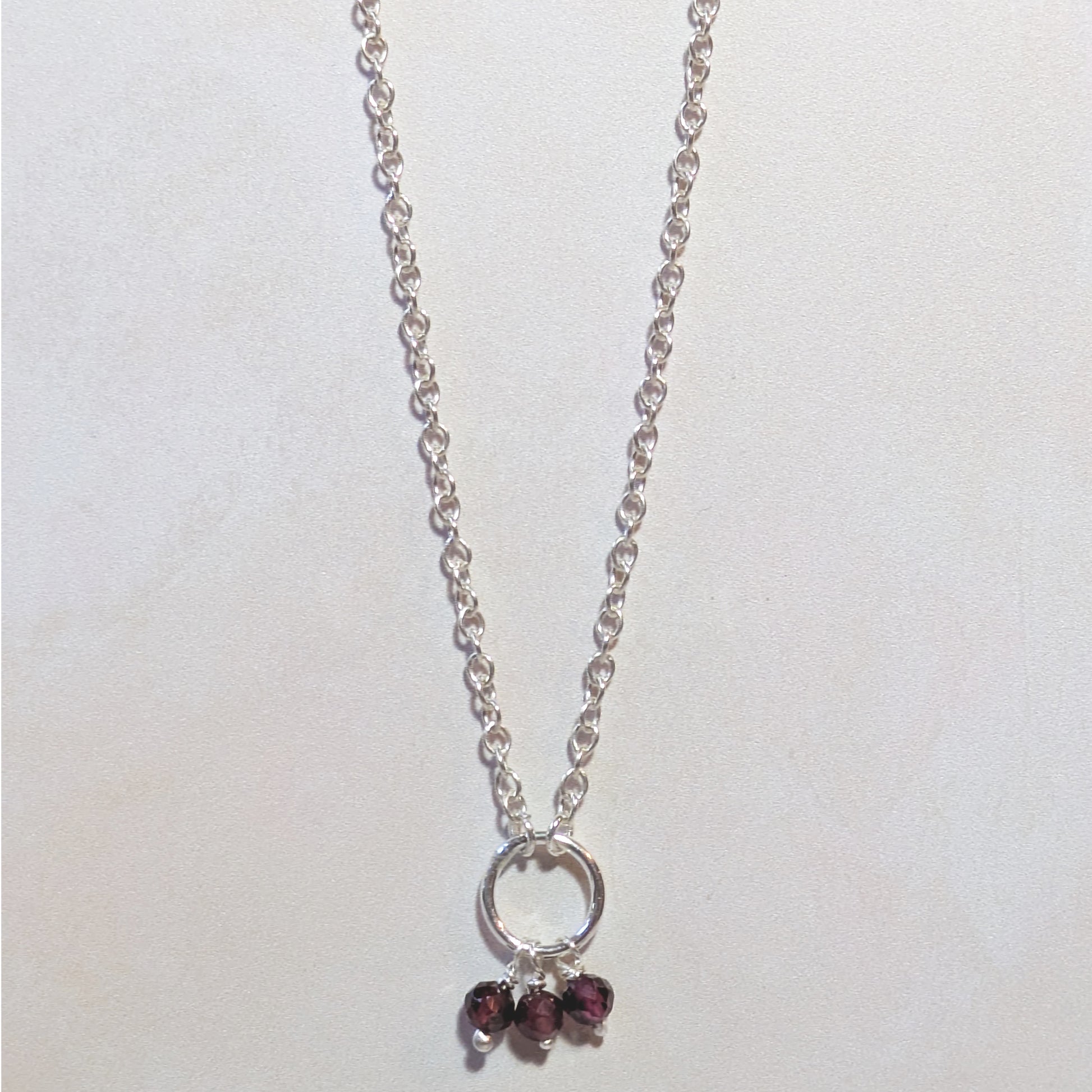 Silver necklace with circular pendant and Garnet gemstone beads on a white background.