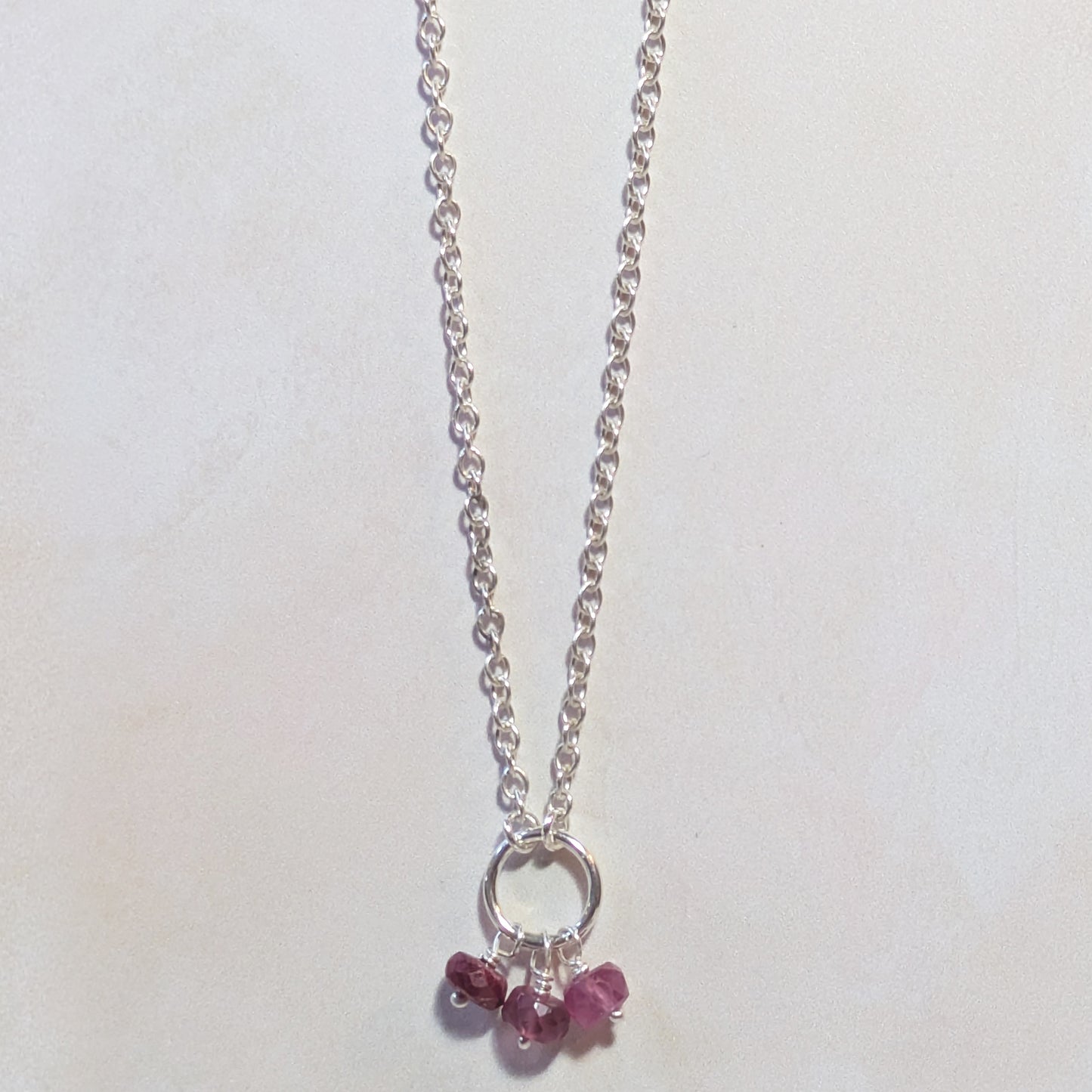Silver necklace with small Ruby gemstone charms on a white background.