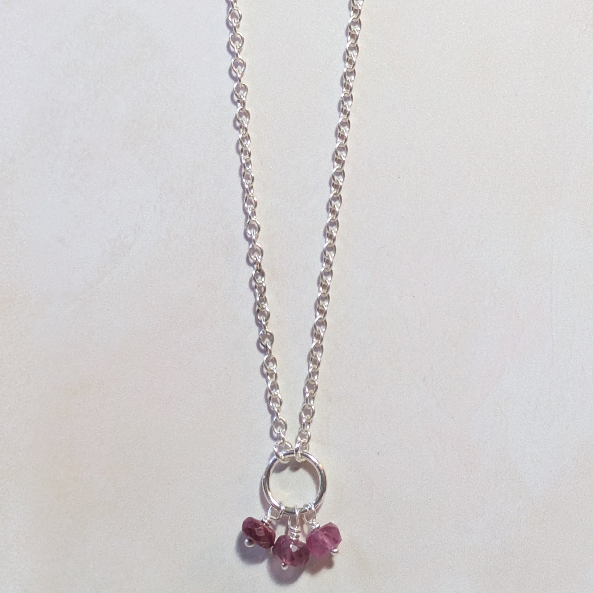 Silver necklace with small Ruby gemstone charms on a white background.