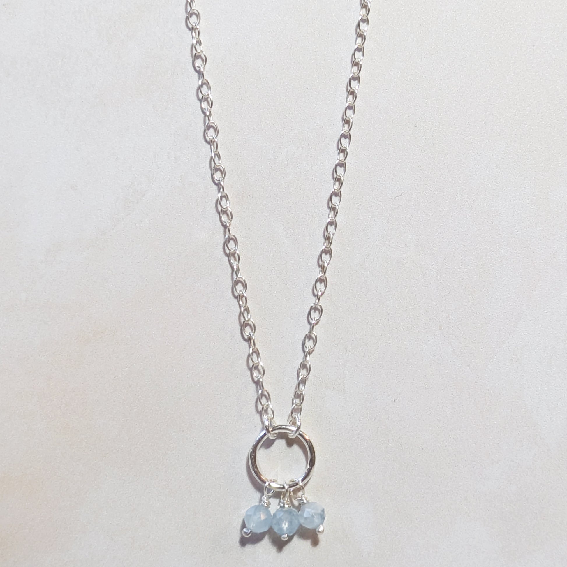 Silver necklace with pale blue Aquamarine gemstone beads on a light grey background.