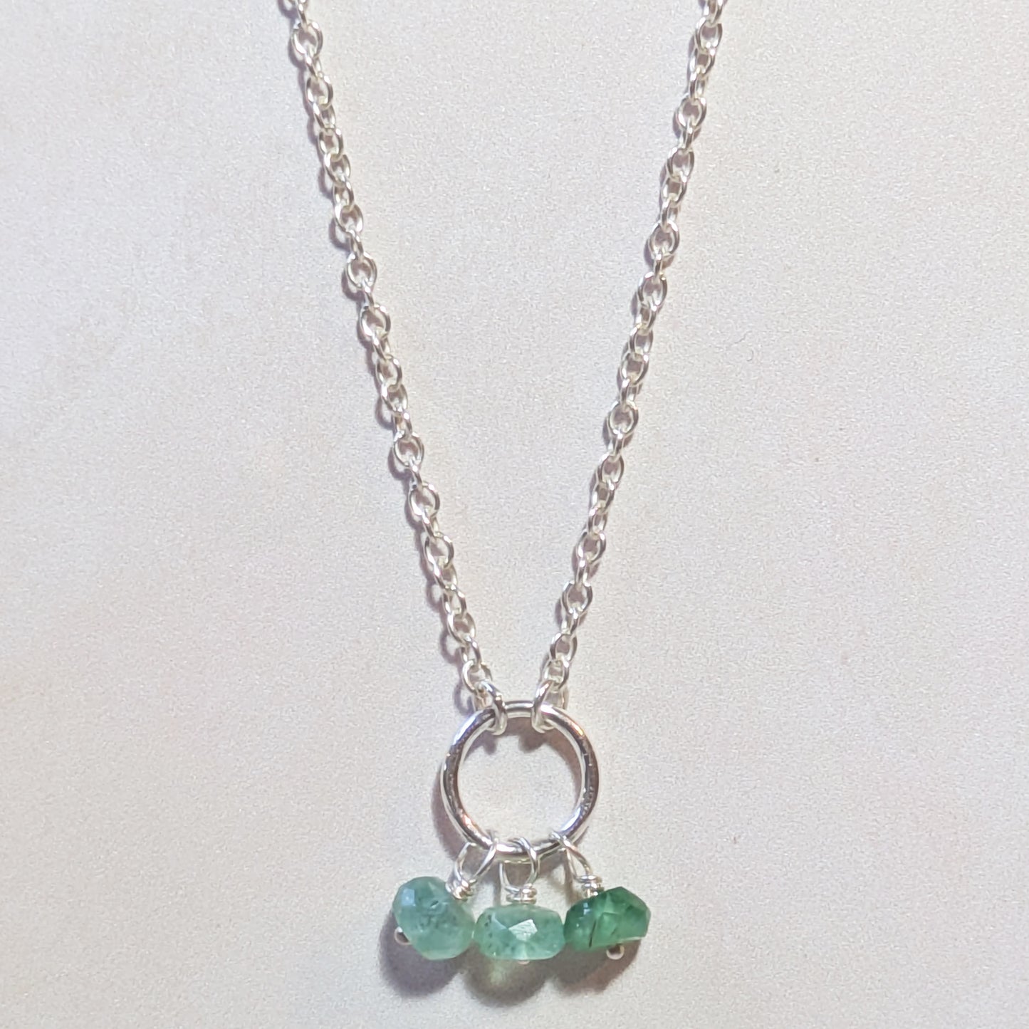 Silver necklace with Emerald gemstones on a white background.