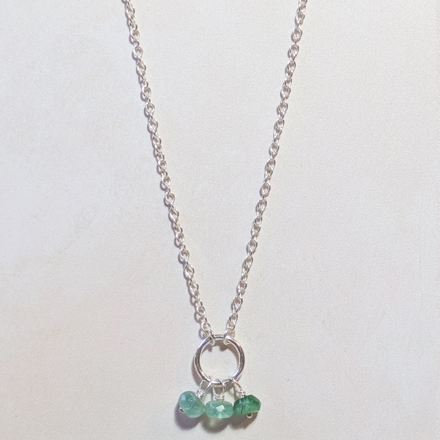 Silver necklace with small circular pendant and Emerald gemstone beads on a white background.