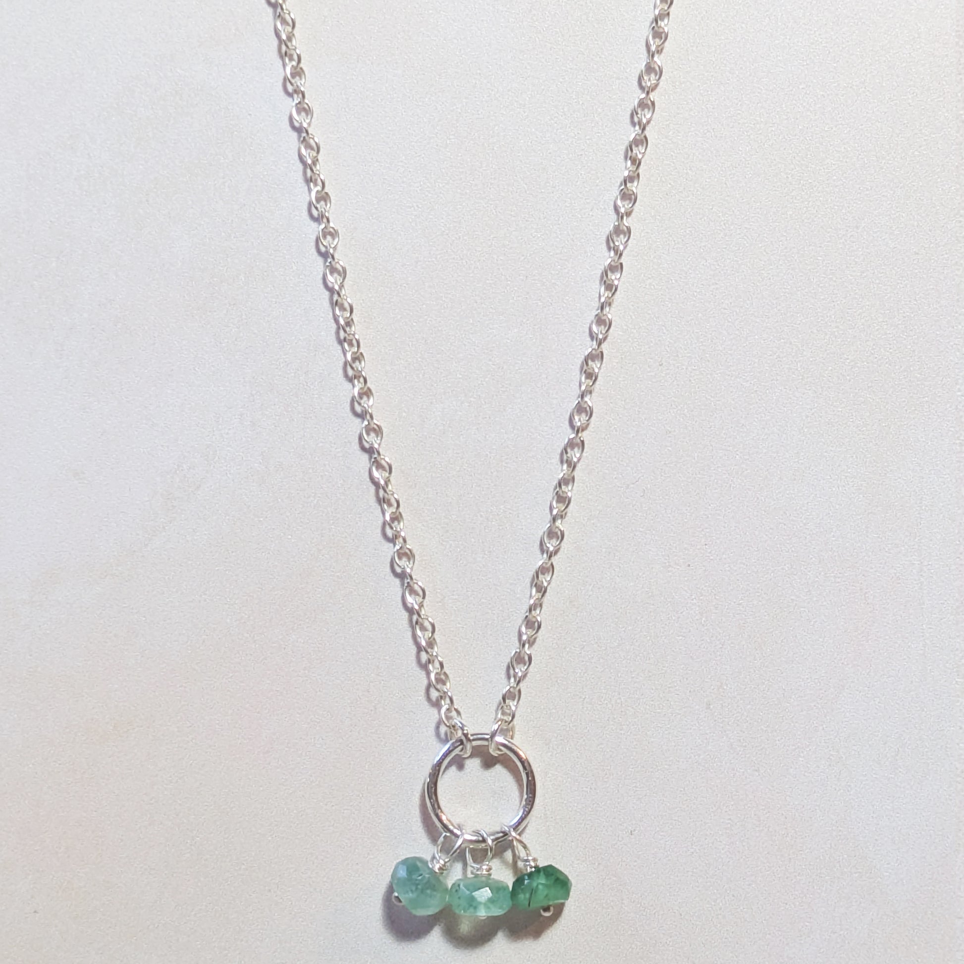Silver necklace with small circular pendant and Emerald gemstone beads on a white background.