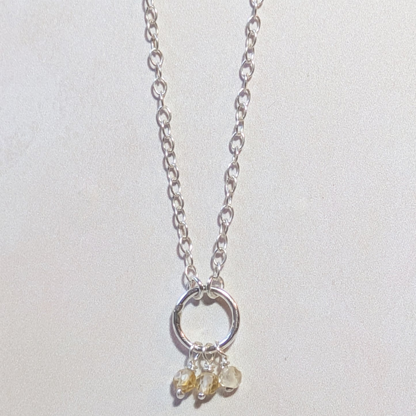 Silver necklace with circular pendant with a Citrine bead cluster on a light neutral background.
