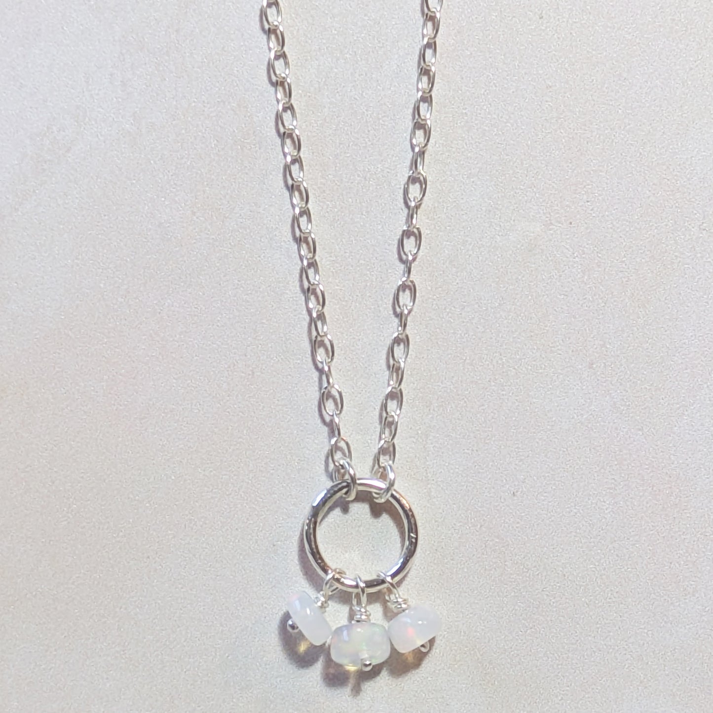 Silver necklace with circular pendant and small Opal gemstone beads on a light grey background.