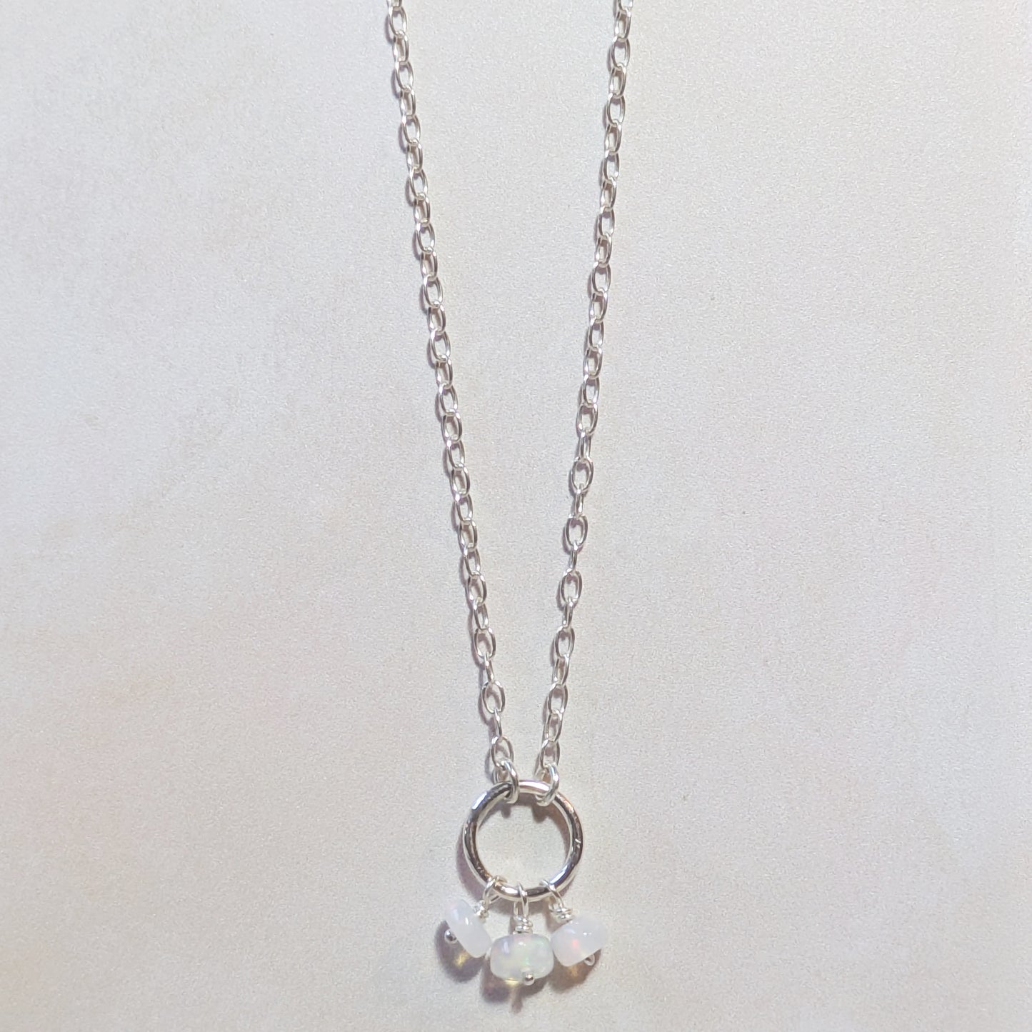 Silver necklace with circular pendant and small Opal beads on a light grey background.