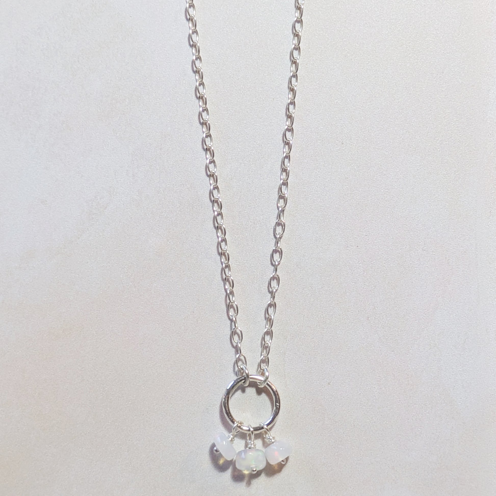 Silver necklace with circular pendant and small Opal beads on a light grey background.