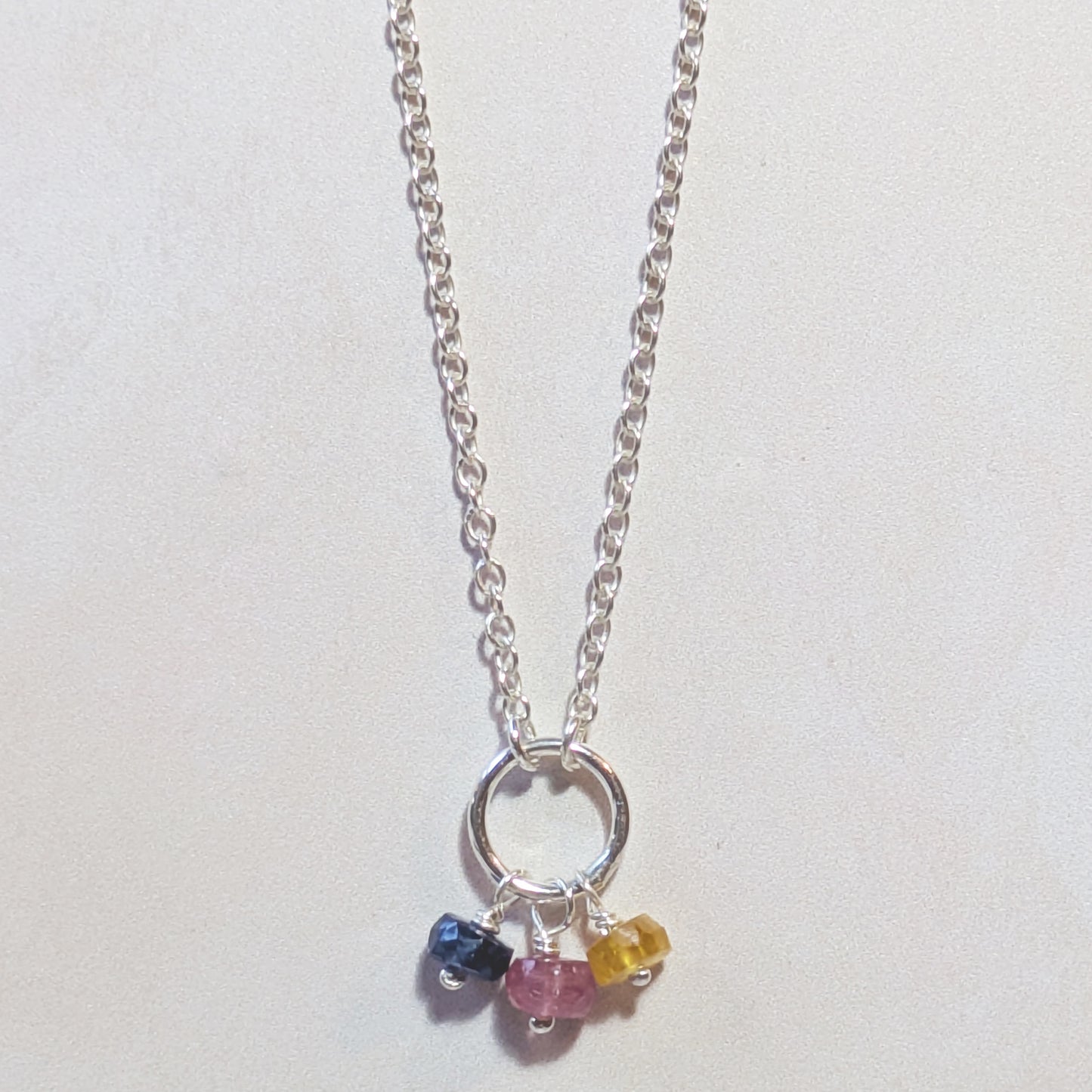 Necklace with multicoloured Sapphire charm on a light background.