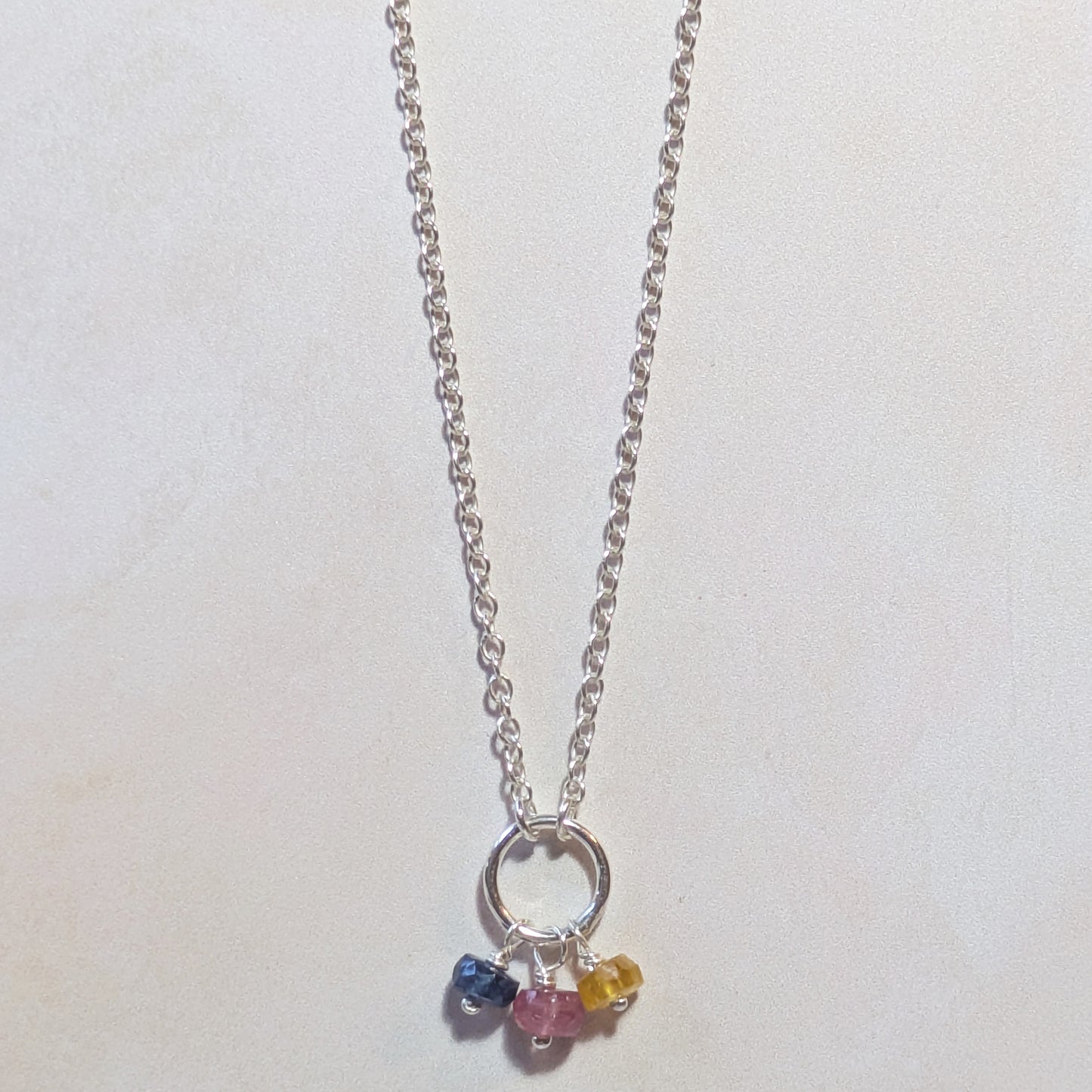 Silver necklace with three multicoloured Sapphire gemstone beads on a white background.