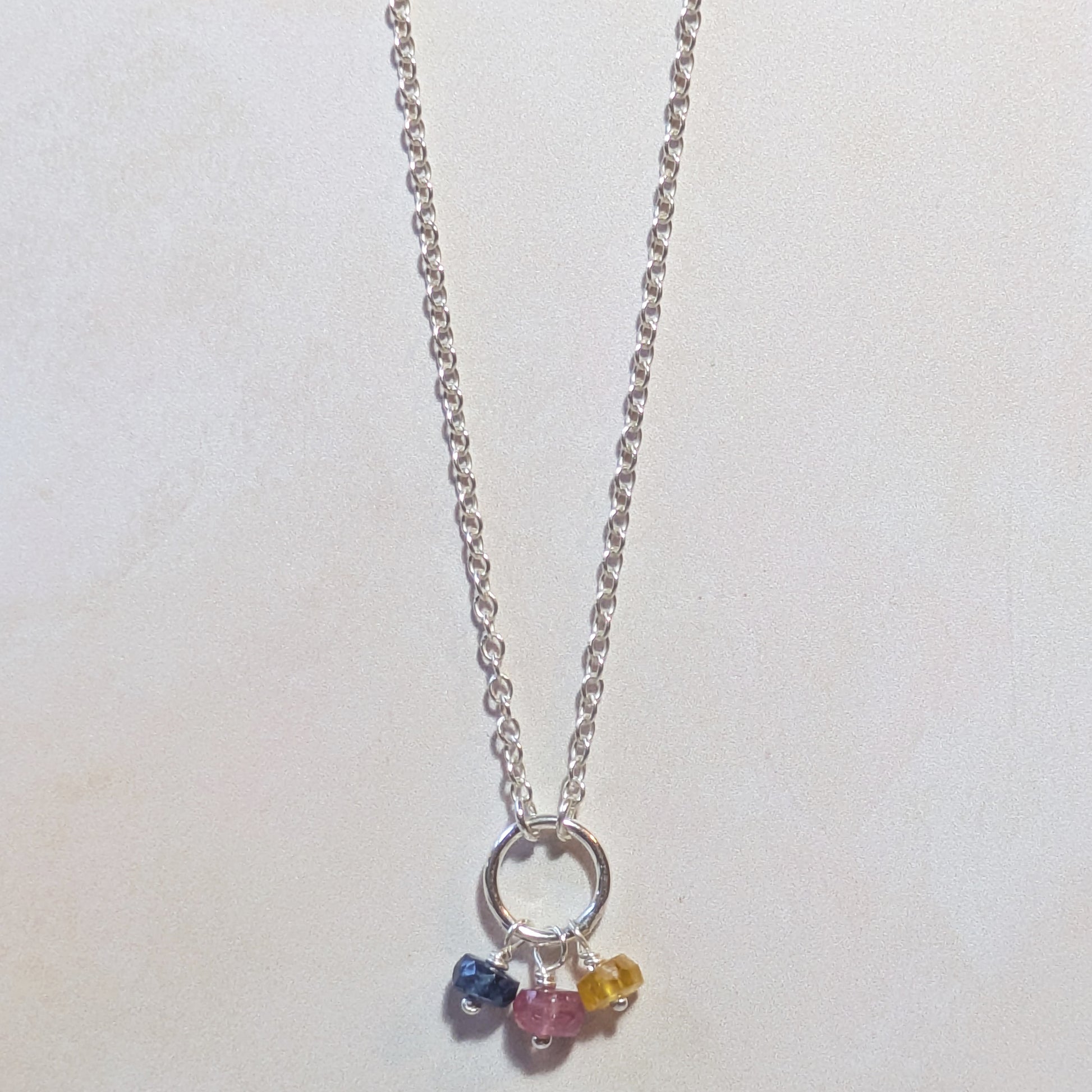 Silver necklace with three multicoloured Sapphire gemstone beads on a white background.