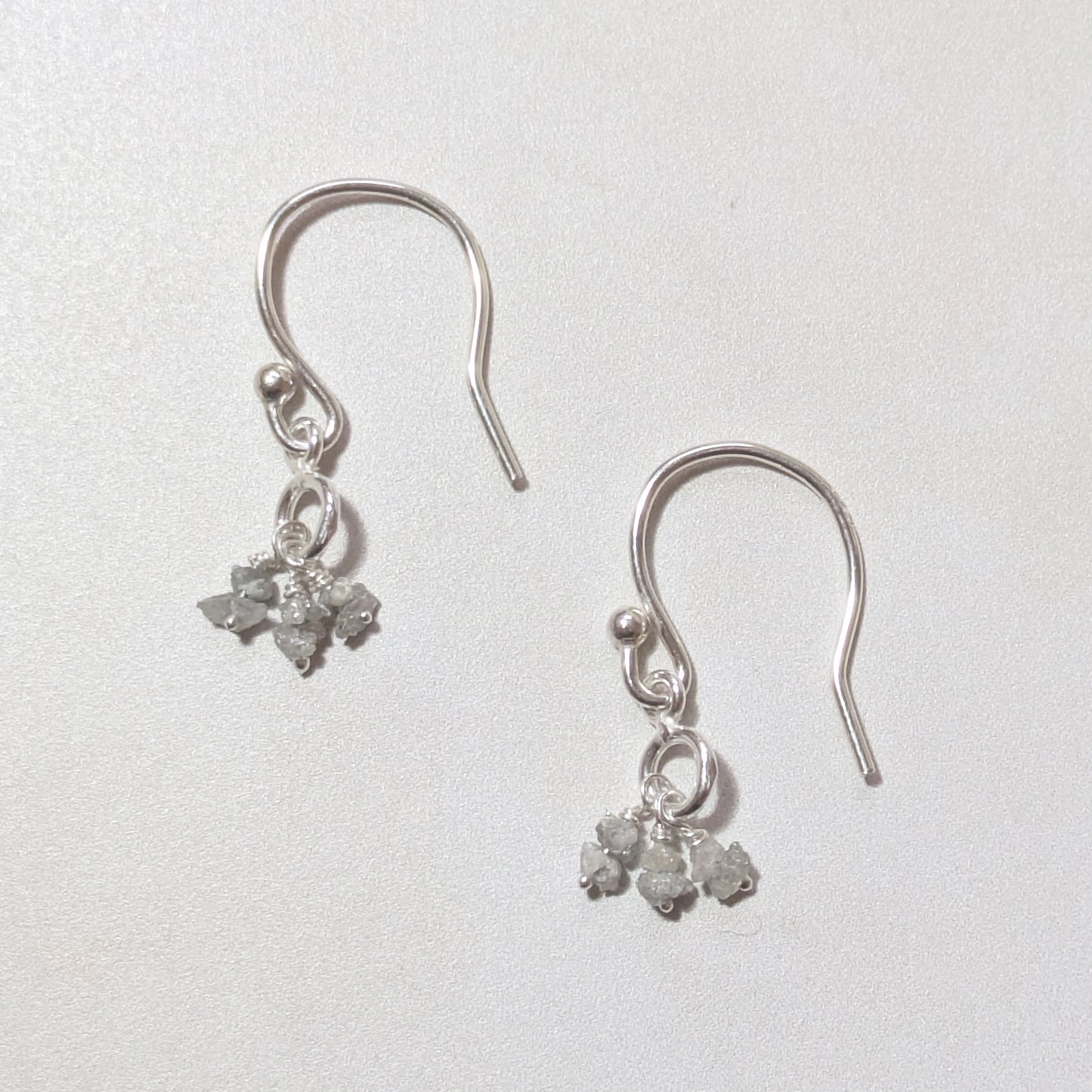 silver hookwire dangly earrings with natural rough Diamond drop charms on a white background.