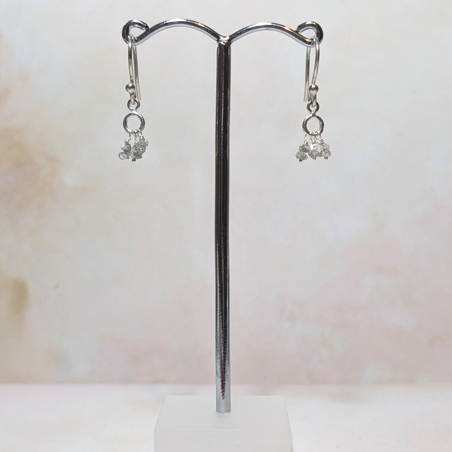 silver drop earrings with rough diamond nuggets on a stand against a neutral background.