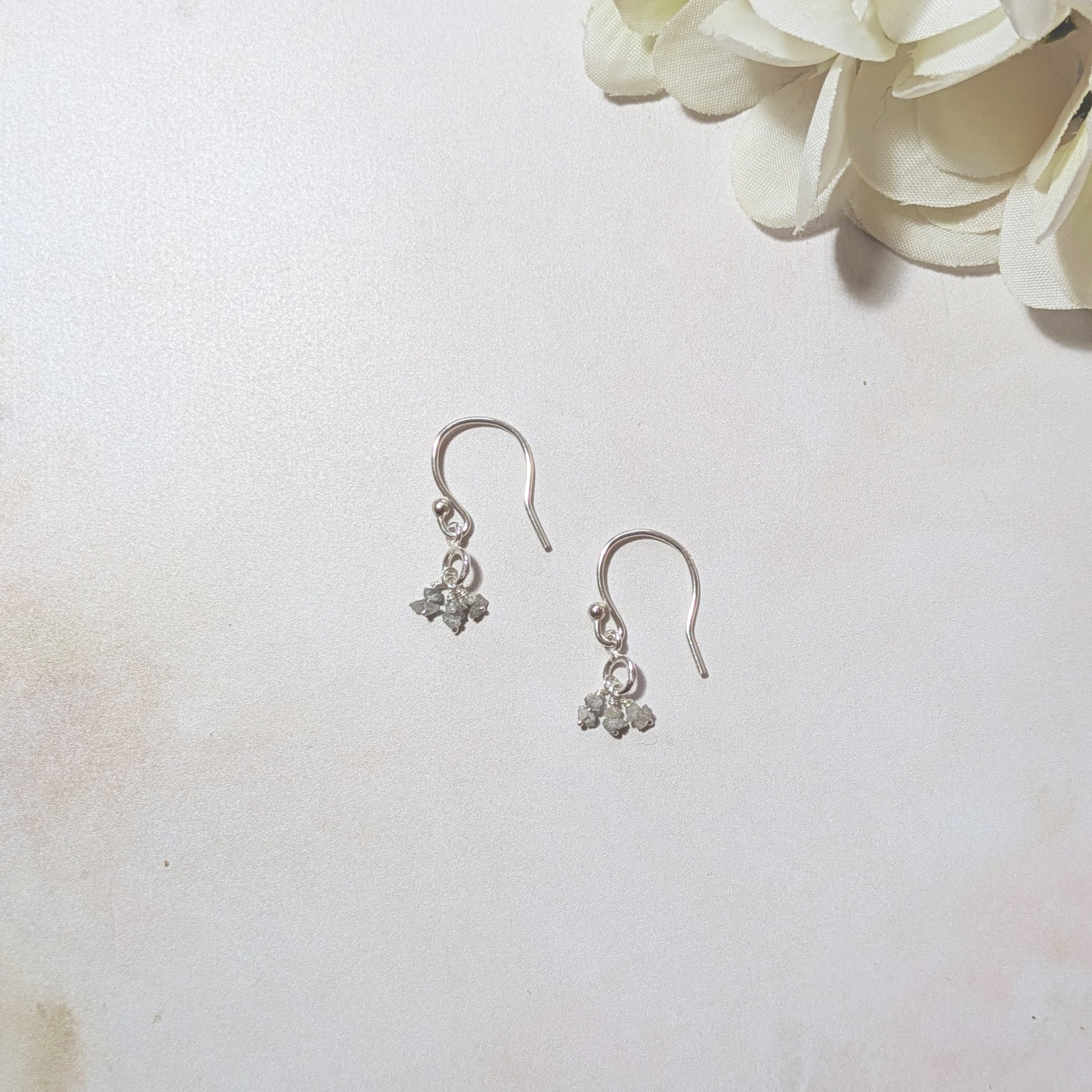 Silver drop earrings with rough Diamond nugget drops on a neutral background.