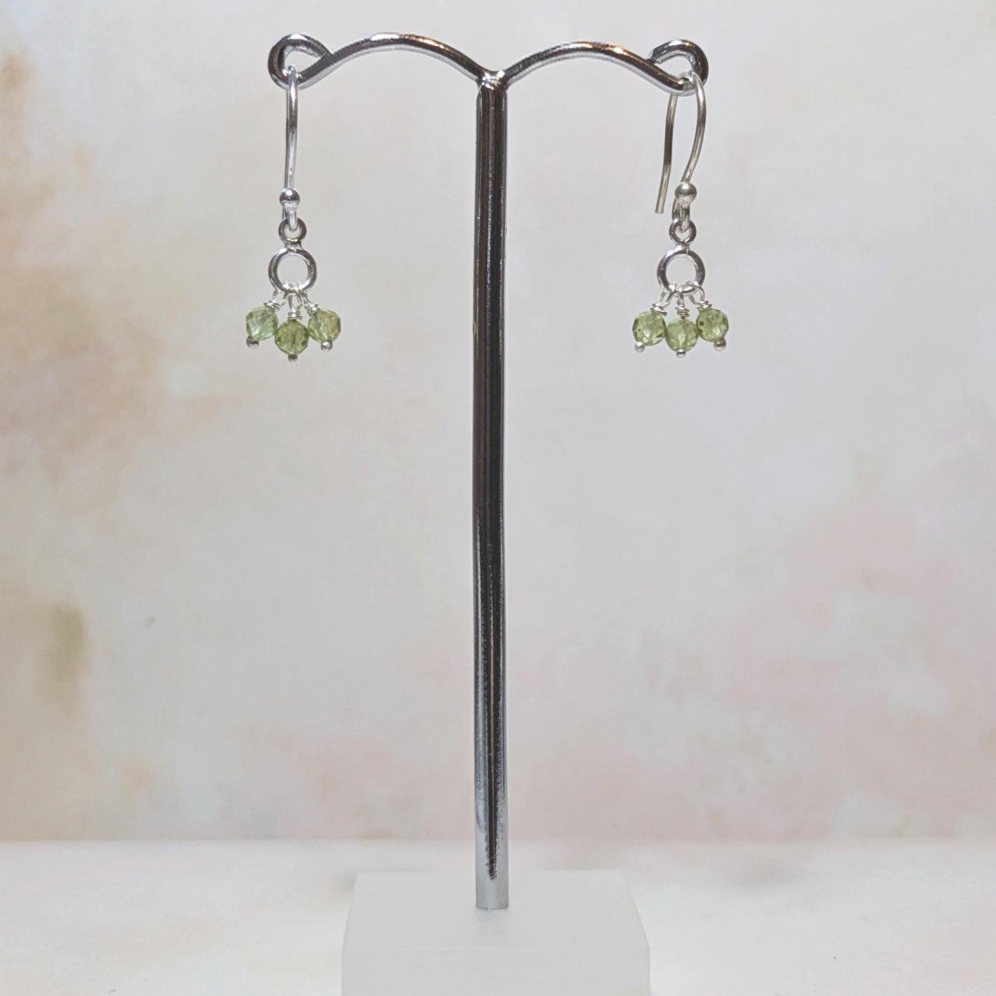 silver drop earrings with peridot beads hanging from a stnd against a neutral background.