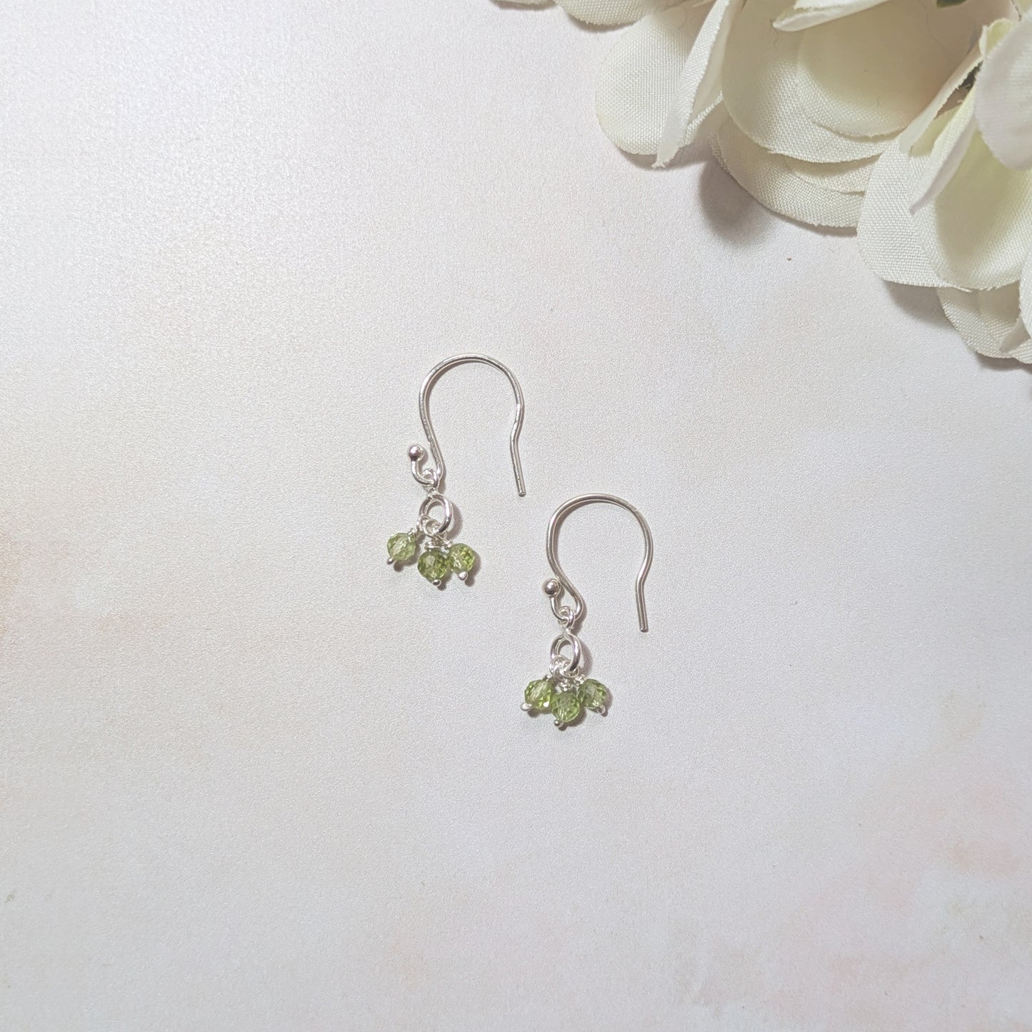 Silver drop earrings with Peridot gemstone beads on a pale background with white flowers.