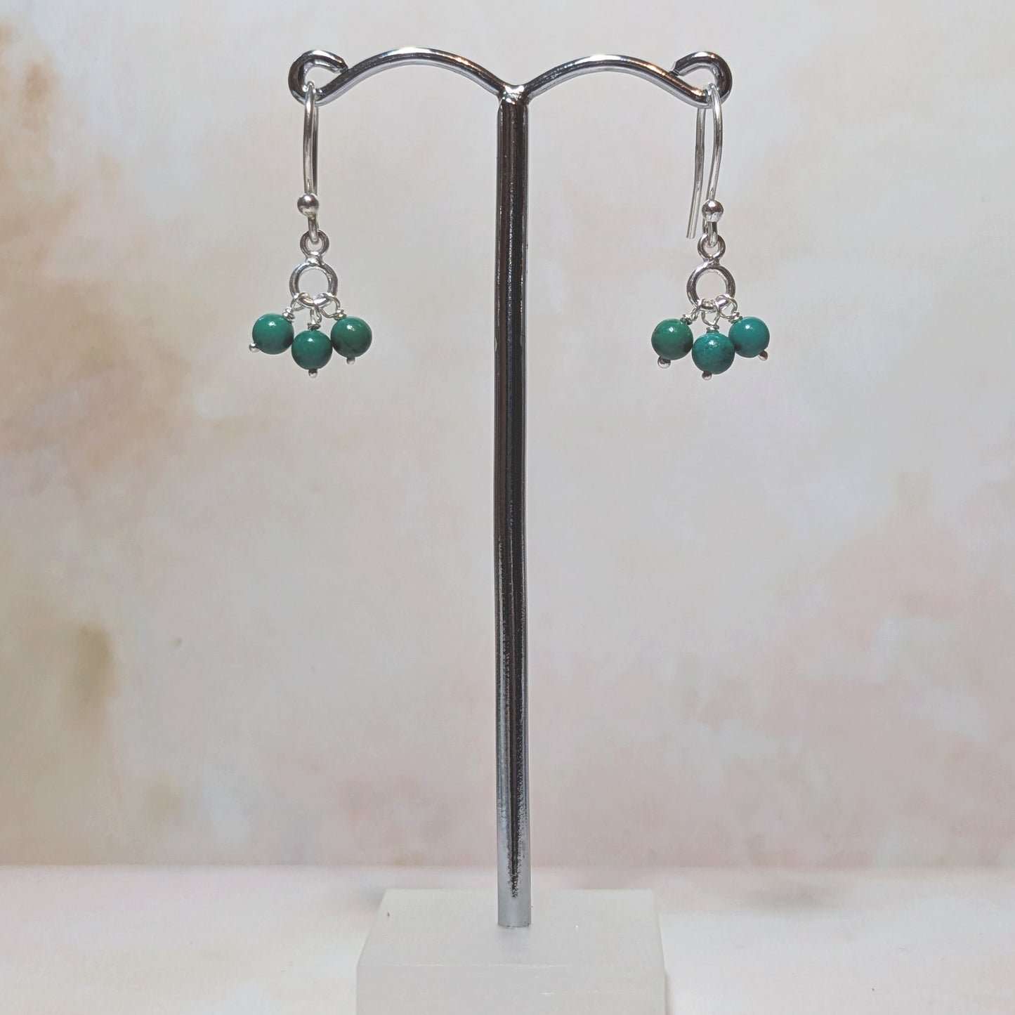 silver hookwire drop earrings with Arizona Turquoise gemstone beads on a stand against a neutral background.