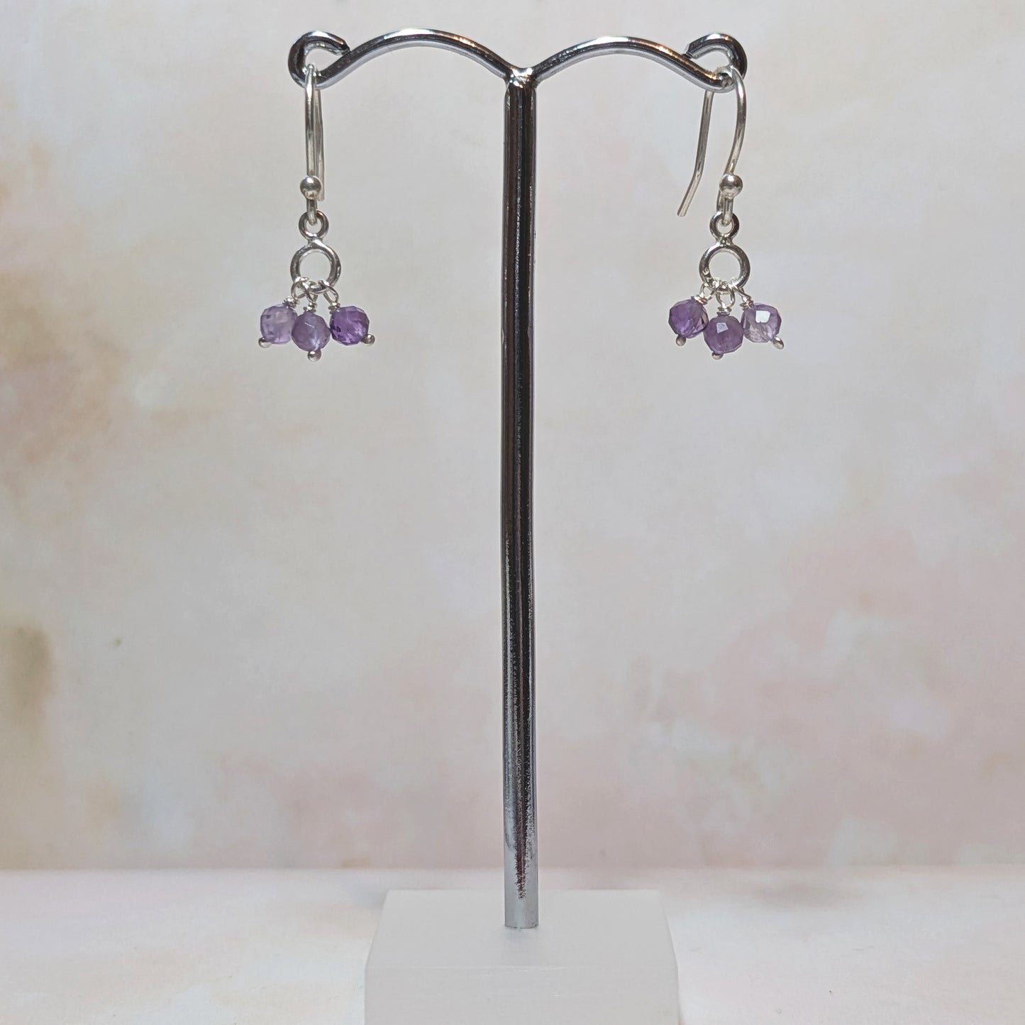 Pair of silver earrings with purple Amethyst beads on a stand against a light background.