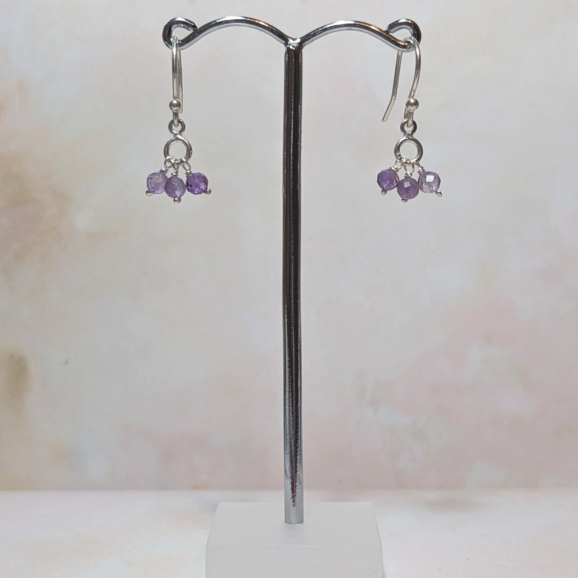 Pair of silver earrings with purple Amethyst beads on a stand against a light background.
