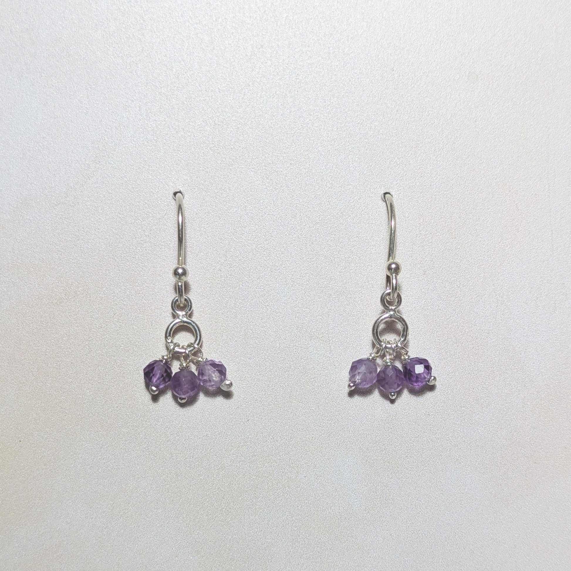 silver drop earrings with purple Amethyst gemstone charms on a neutral background.