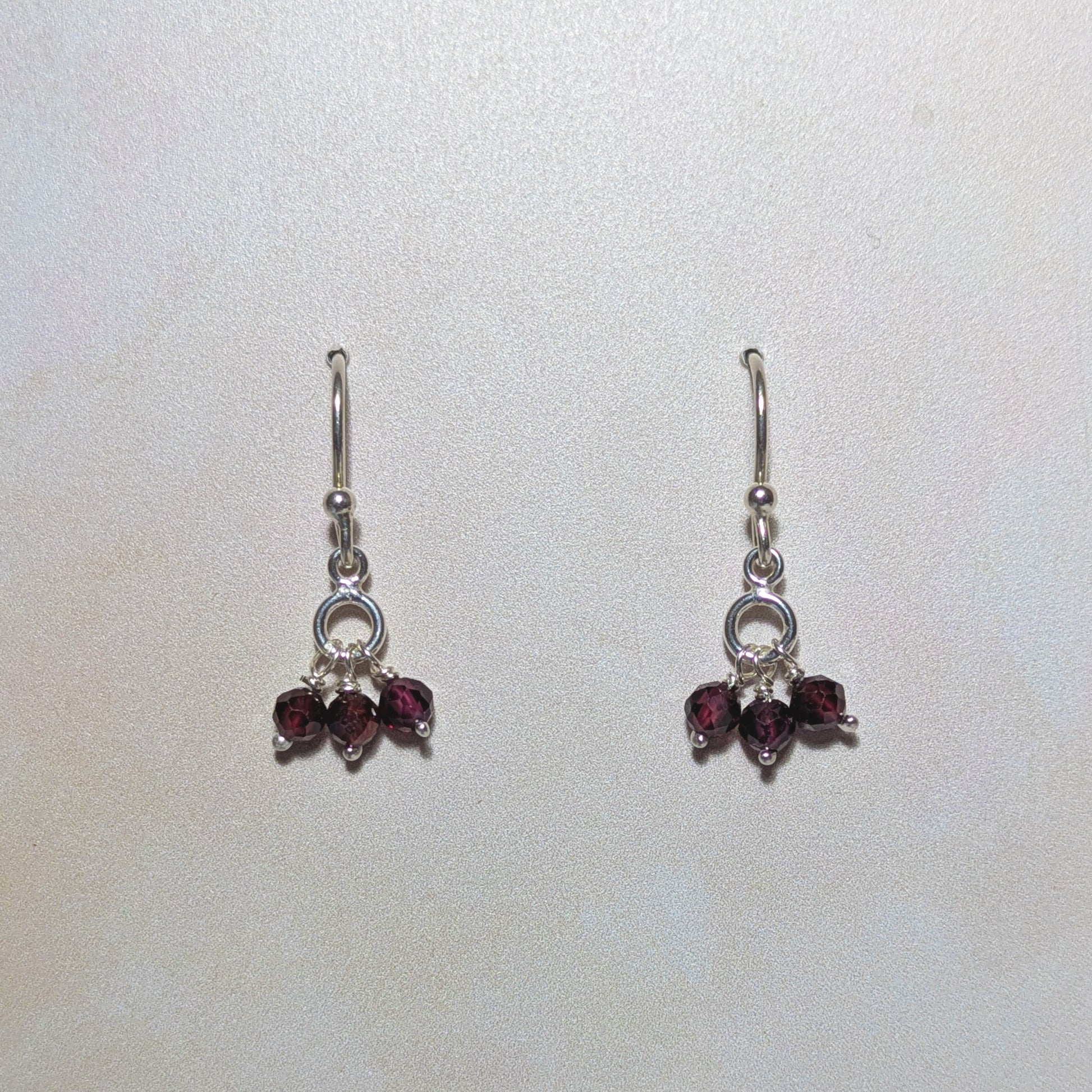 Pair of silver earrings with red Garnet gemstones on a white background.
