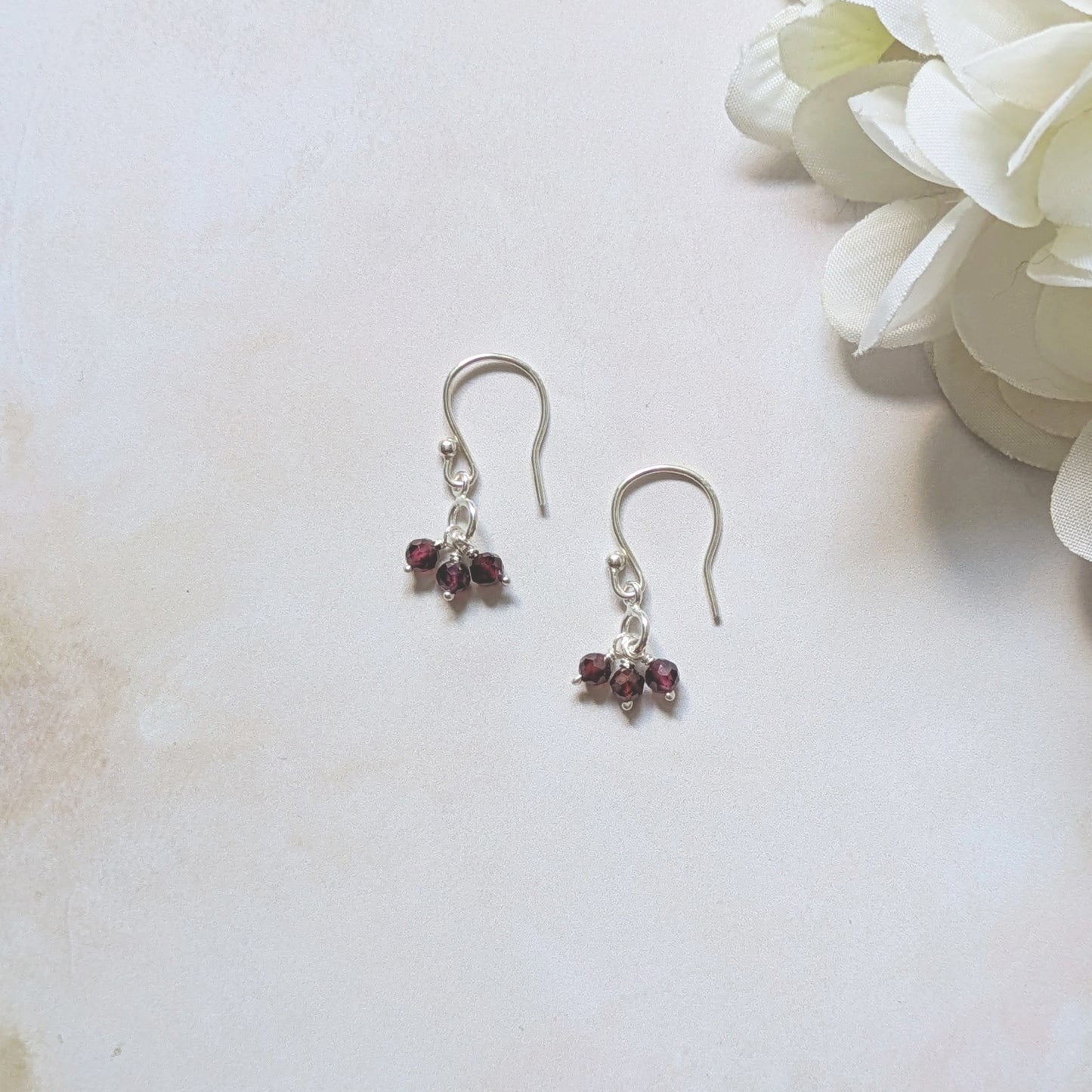 Silver drop earrings with Garnet gemstone beads on a light background with a white flower.