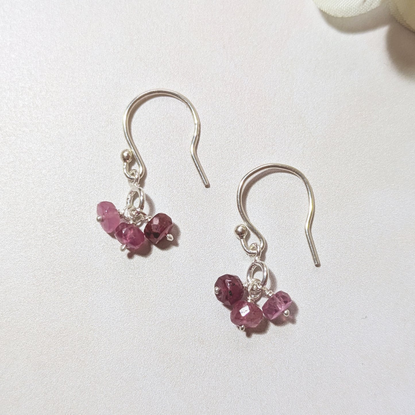 Silver dangly earrings with Ruby gemstone charms on a white background.