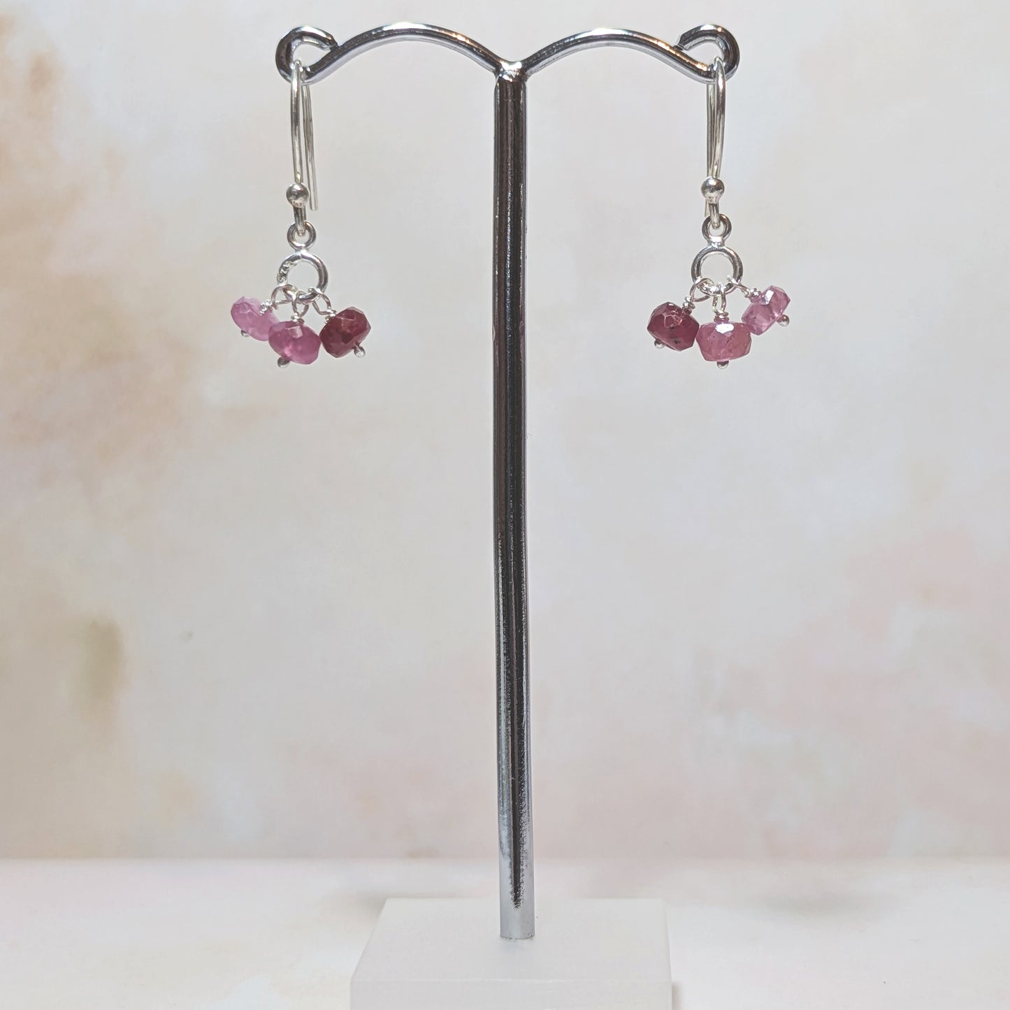 Pair of earrings with Rubies on a stand against a white background.