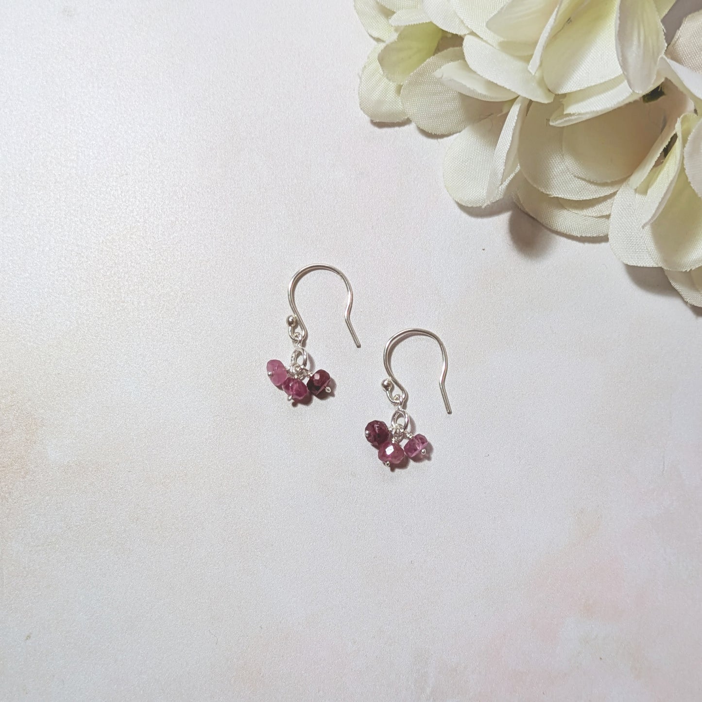 Silver drop earrings with Ruby gemstones on a white background with flowers.