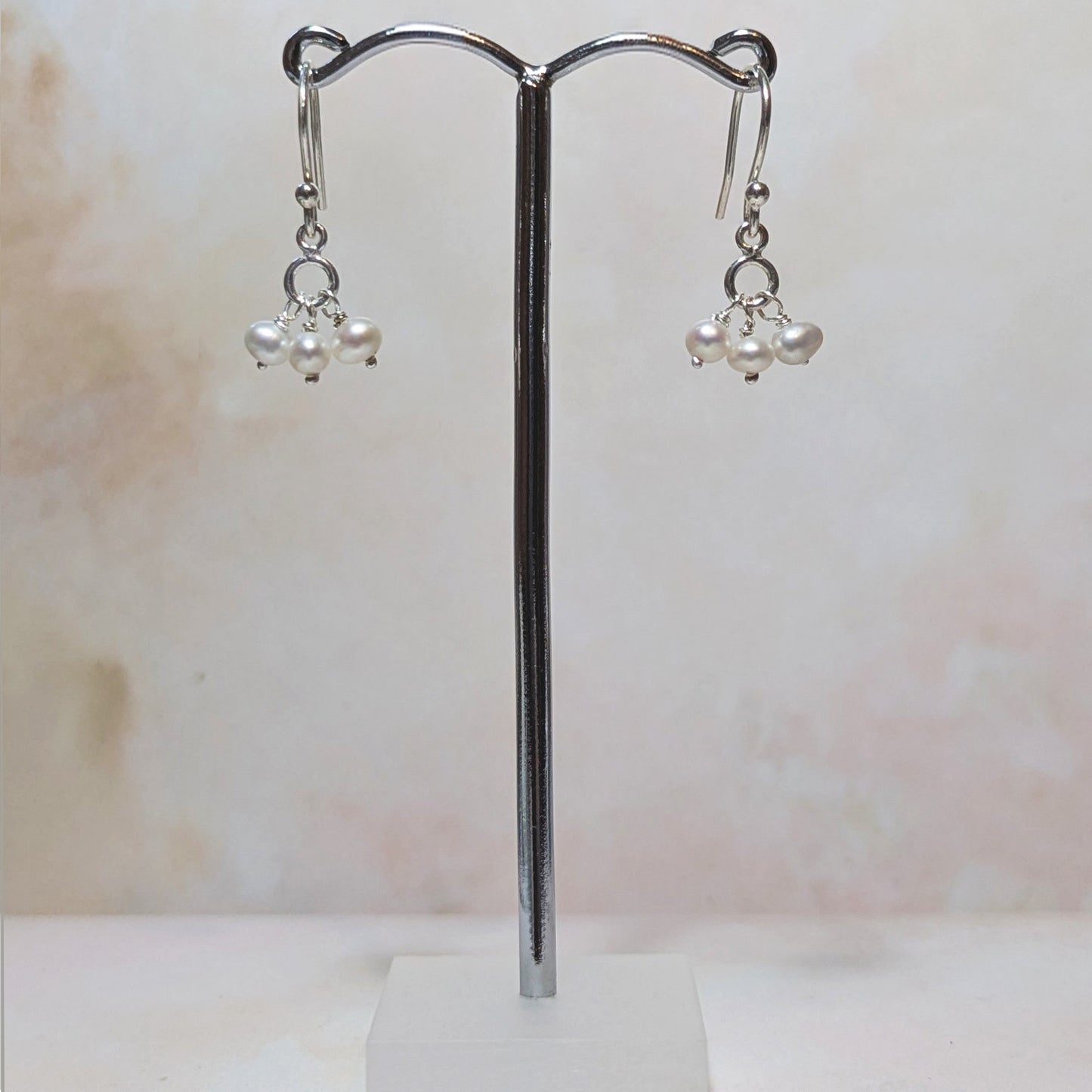 Pair of pearl earrings on a stand against a marble background