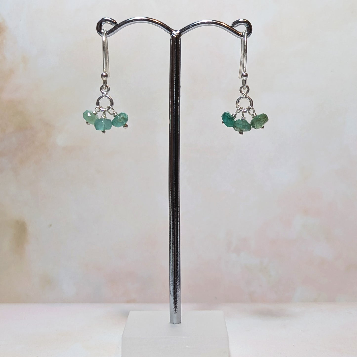 Pair of earrings with Emerald gemstone beads on a stand against a light background.