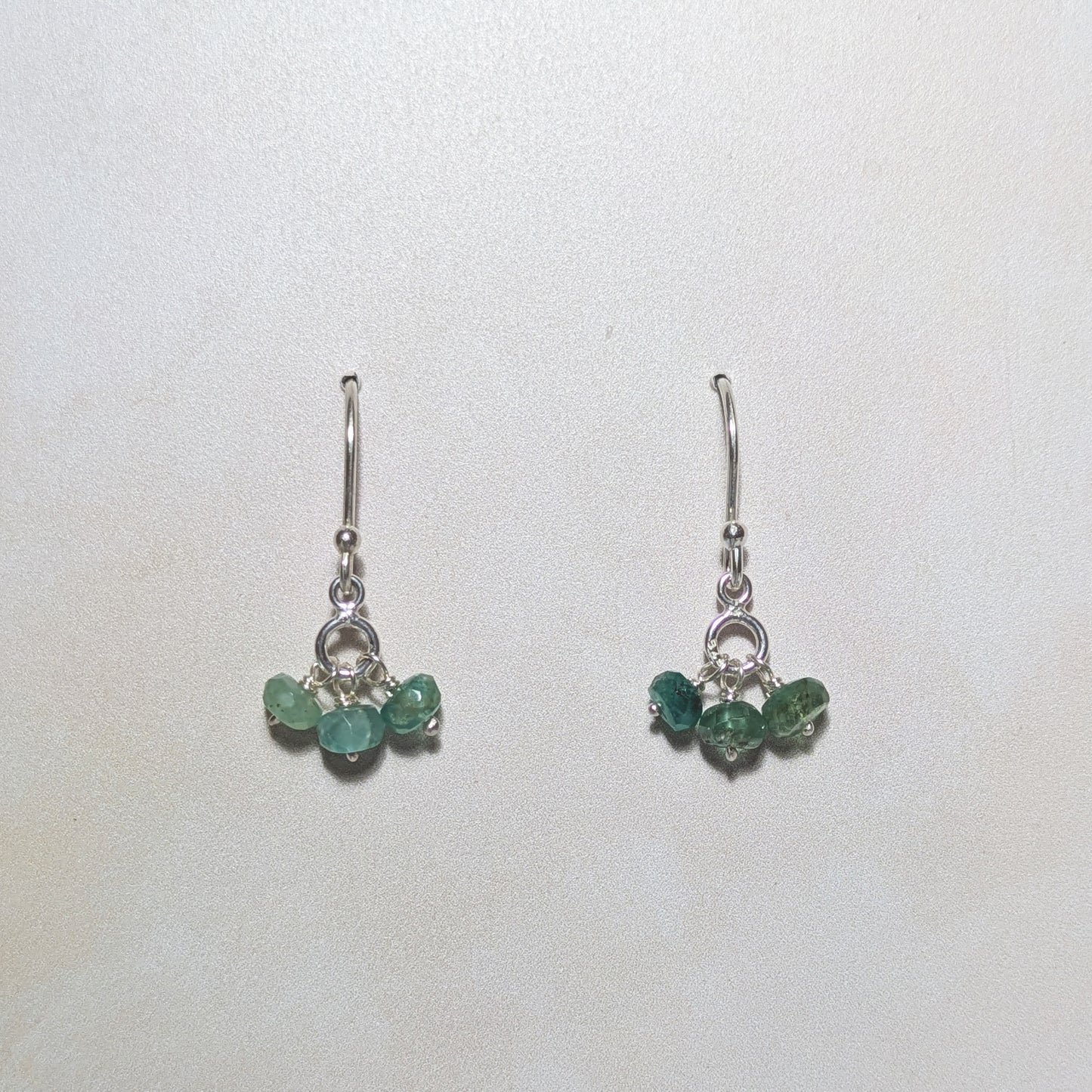 Pair of silver earrings with Emerald gemstone bead drops on a white background.