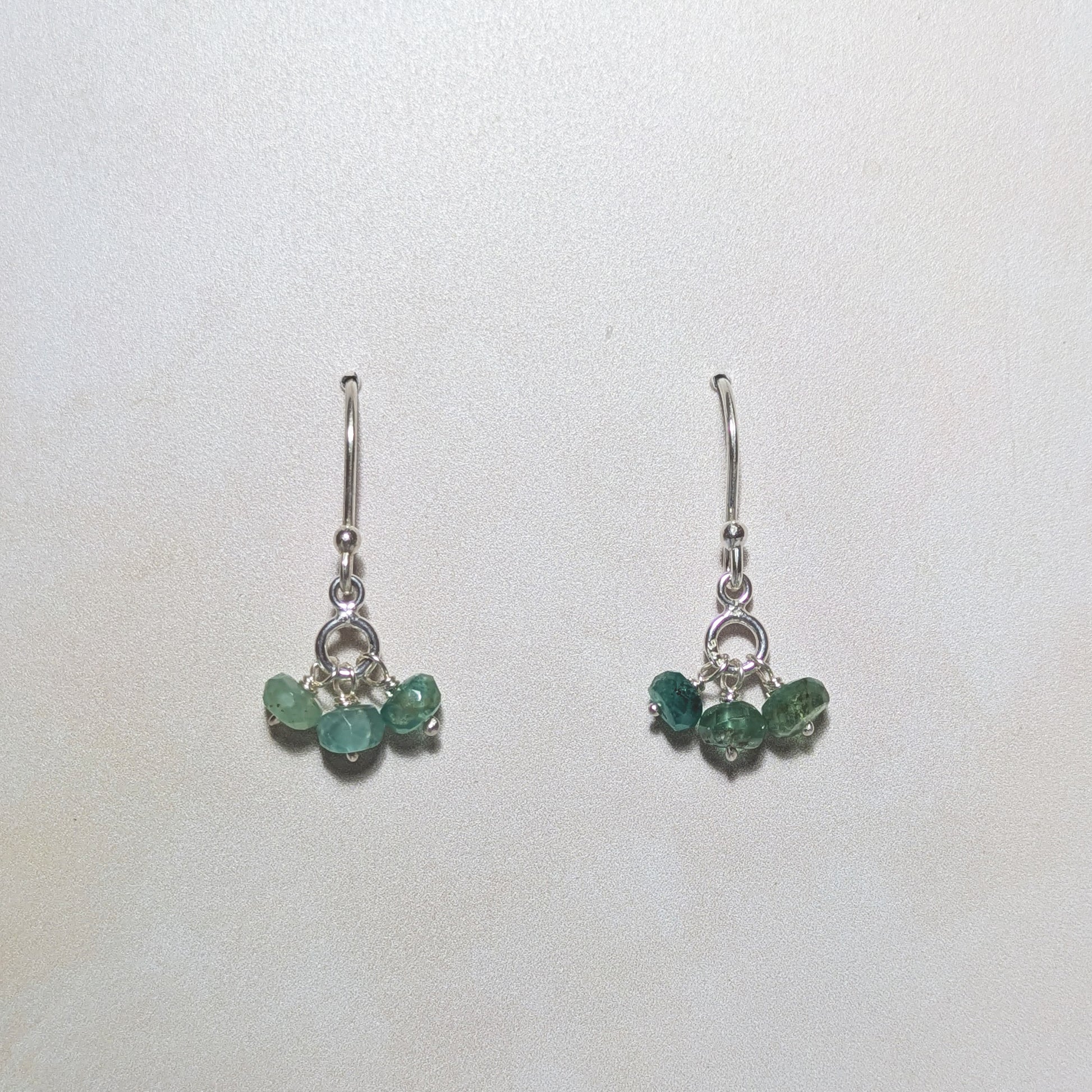 Pair of silver earrings with Emerald gemstone bead drops on a white background.