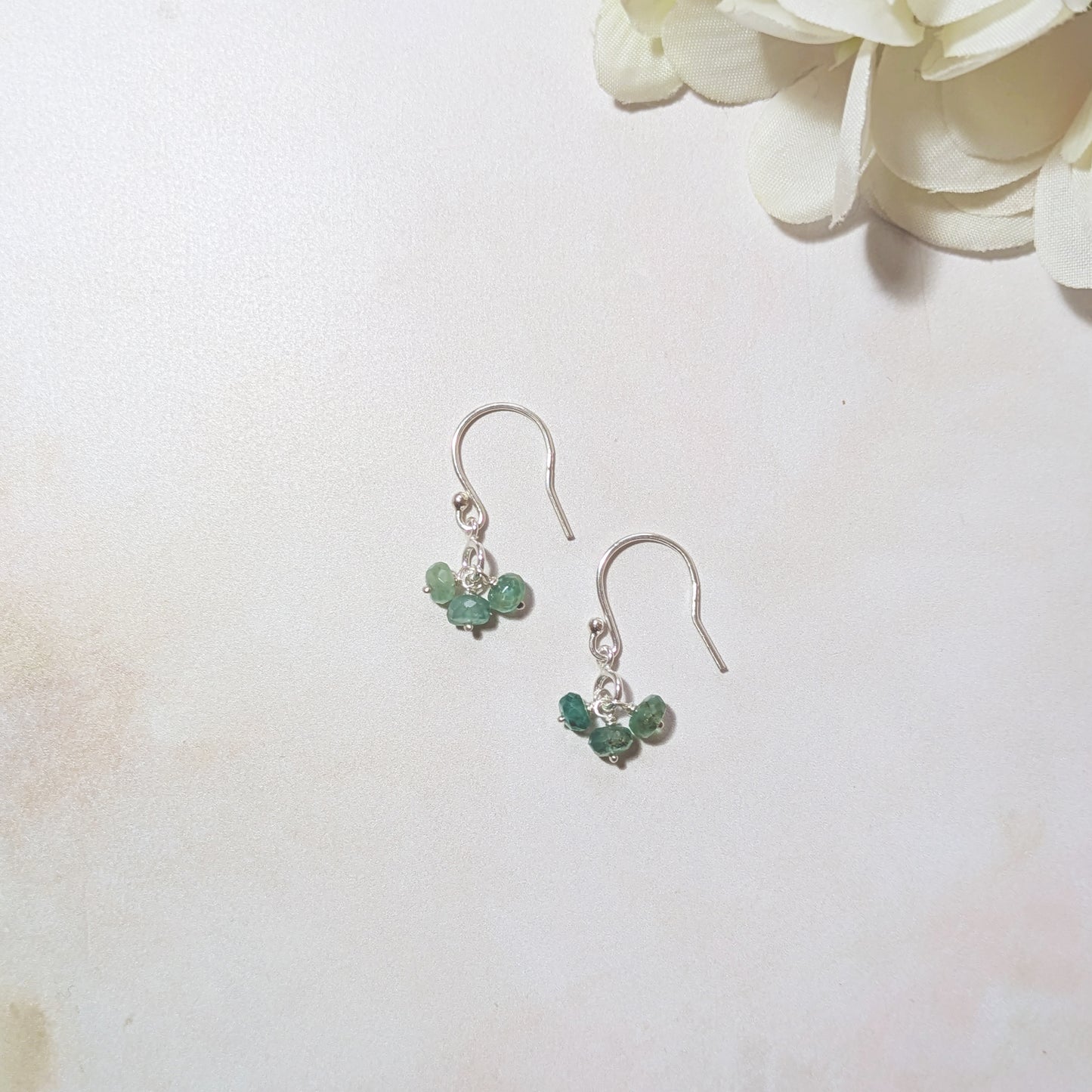 Silver earrings with green Emerald gemstones on a white background with flowers.