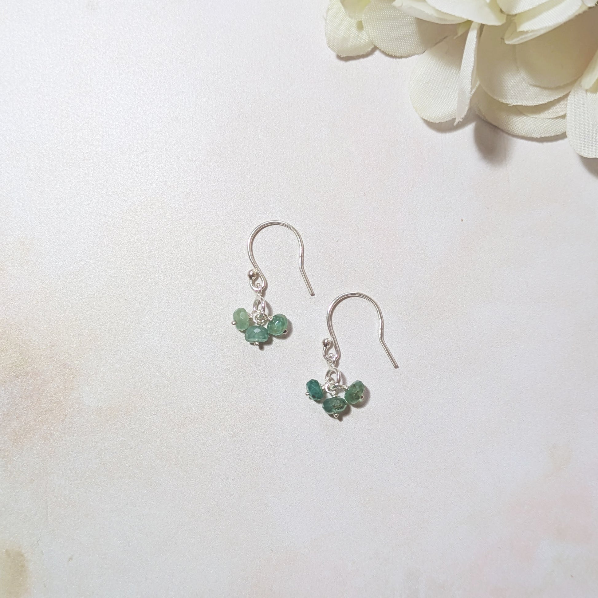 Silver earrings with green Emerald gemstones on a white background with flowers.