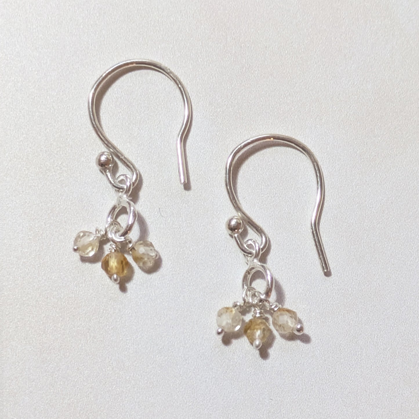 Silver earrings with mini Citrine gemstones on a light grey background.