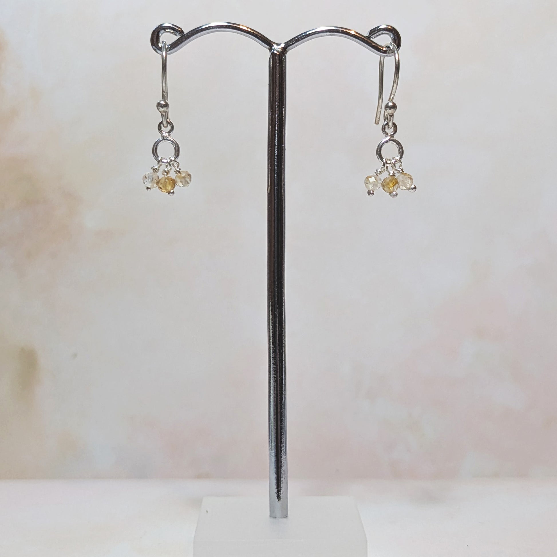 silver drop earrings with Citrine charms hanging from a stand against a neutral background.
