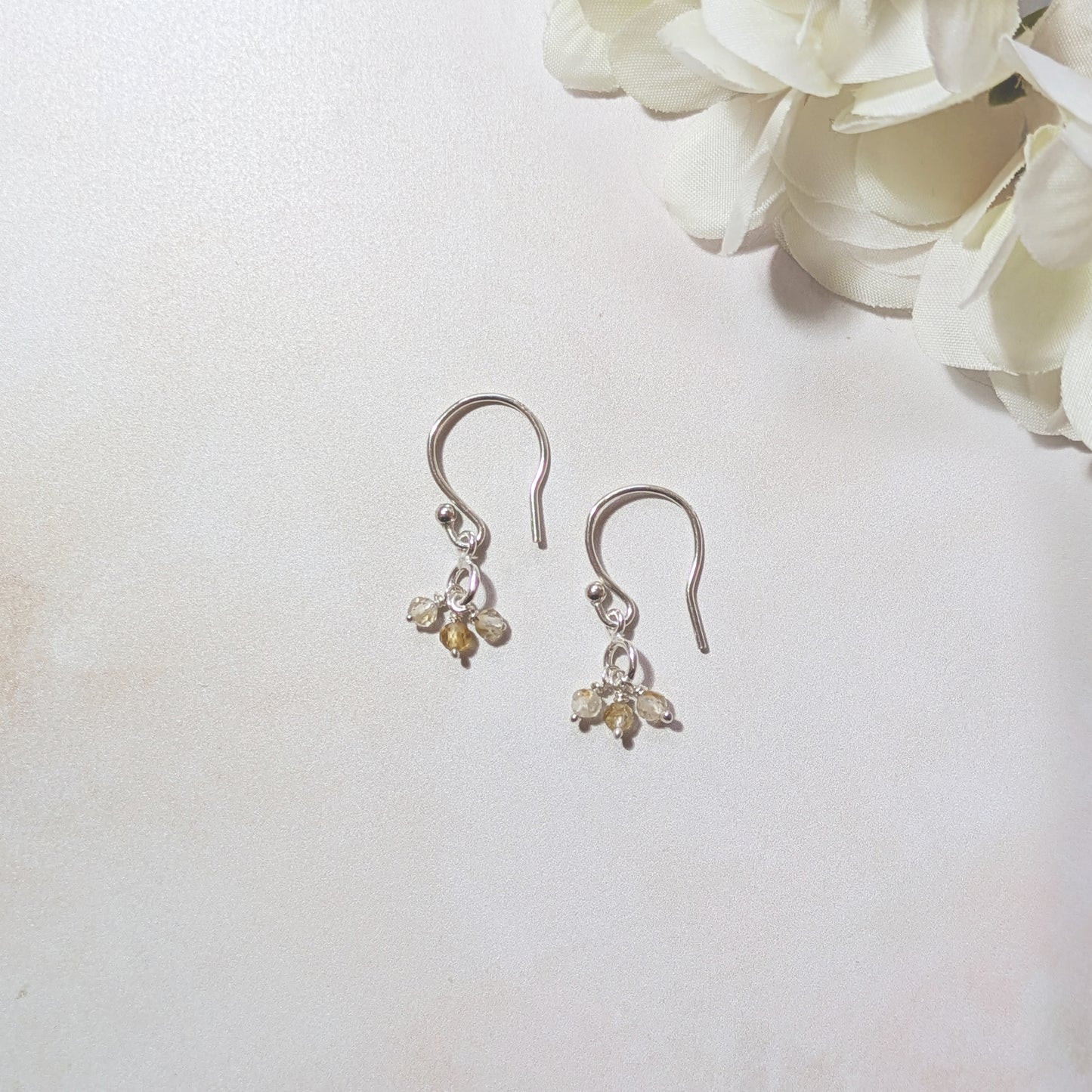 Pair of silver earrings with small Citrine gemstone drops on a white background with flowers.
