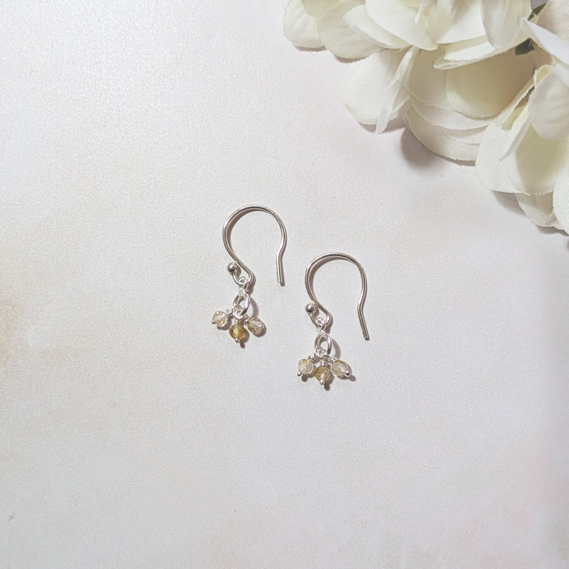 Pair of silver earrings with small Citrine gemstone drops on a white background with flowers.