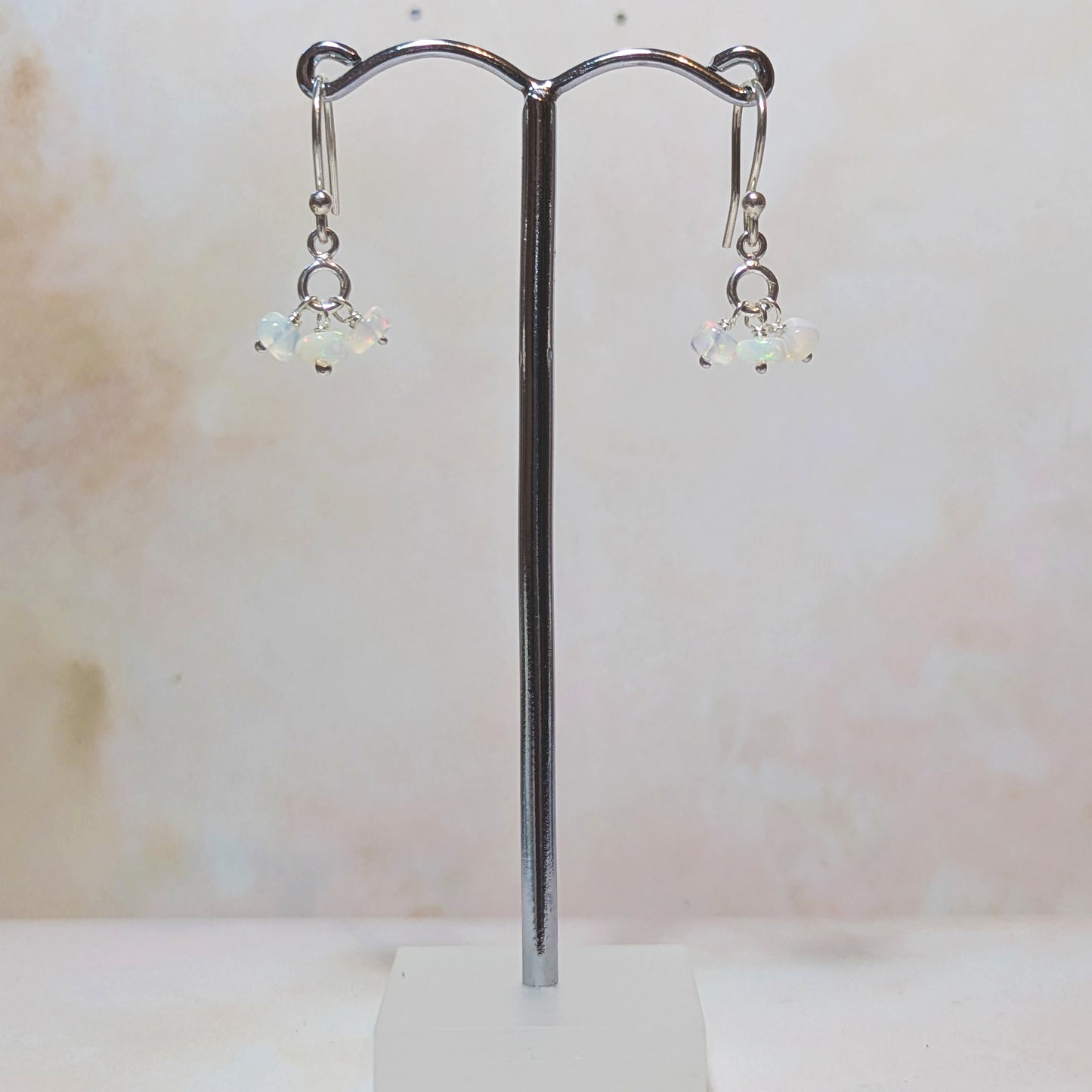 silver drop earrings with Opal gemstone charms hanging from a stand against a neutral background.