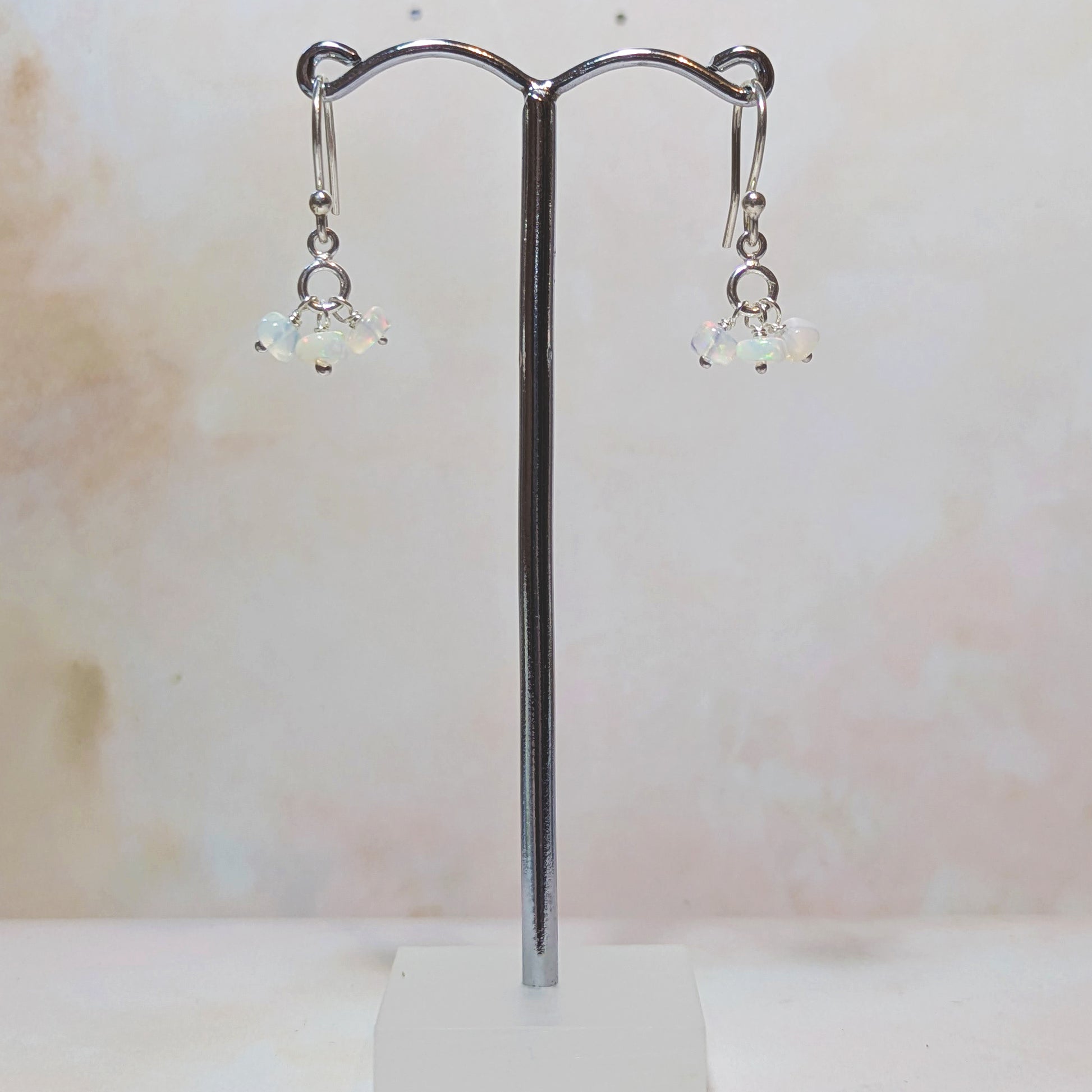 silver drop earrings with Opal gemstone charms hanging from a stand against a neutral background.