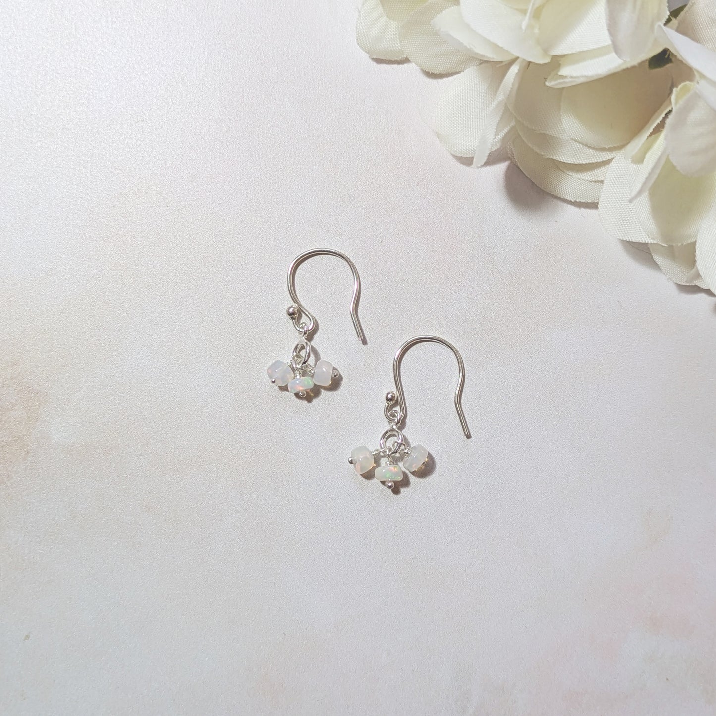 Silver dangling earrings with Opal gemstones on a neutral background with white flowers.