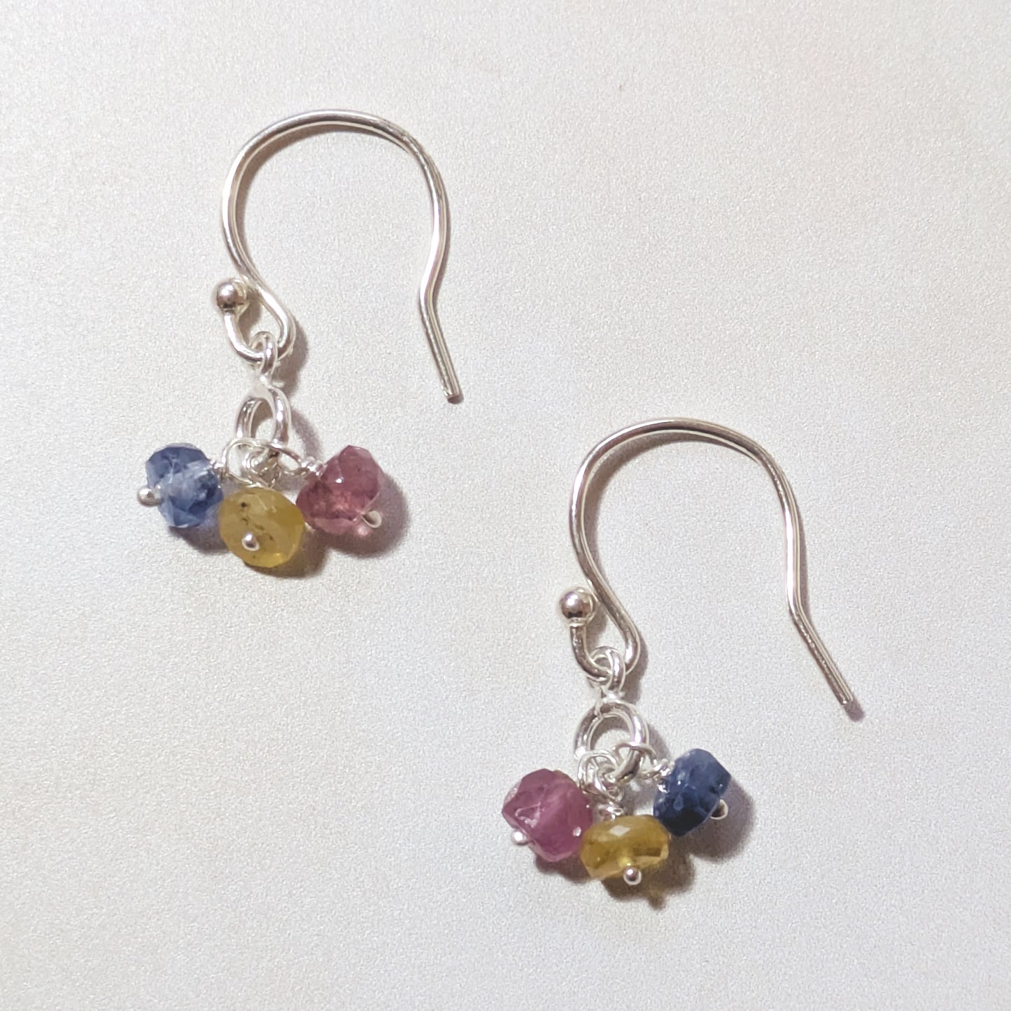 Silver drop earrings with multicoloured Sapphire gemstones on a white background.